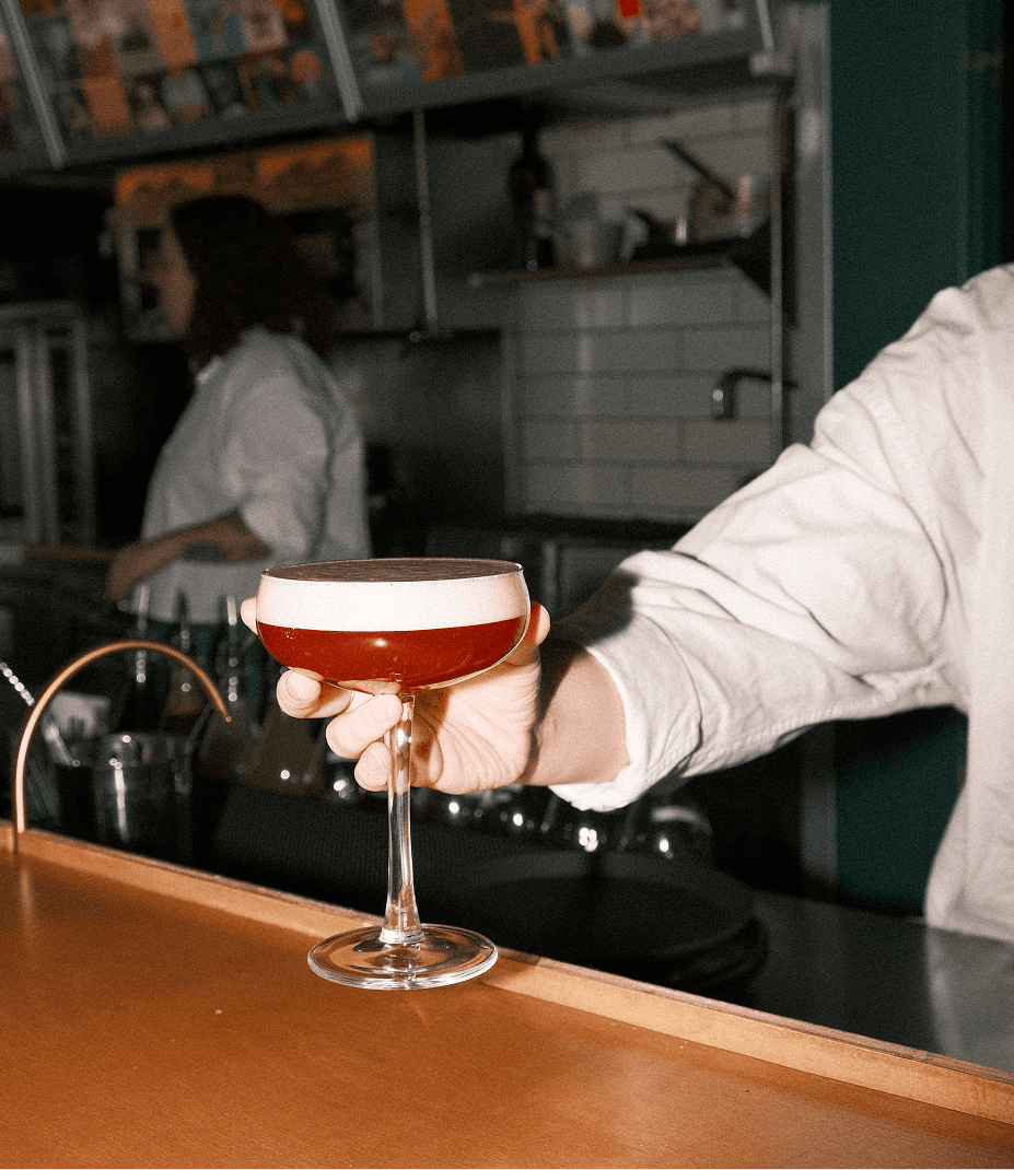 Une serveuse tiens un cocktail rouge à bout de bras.