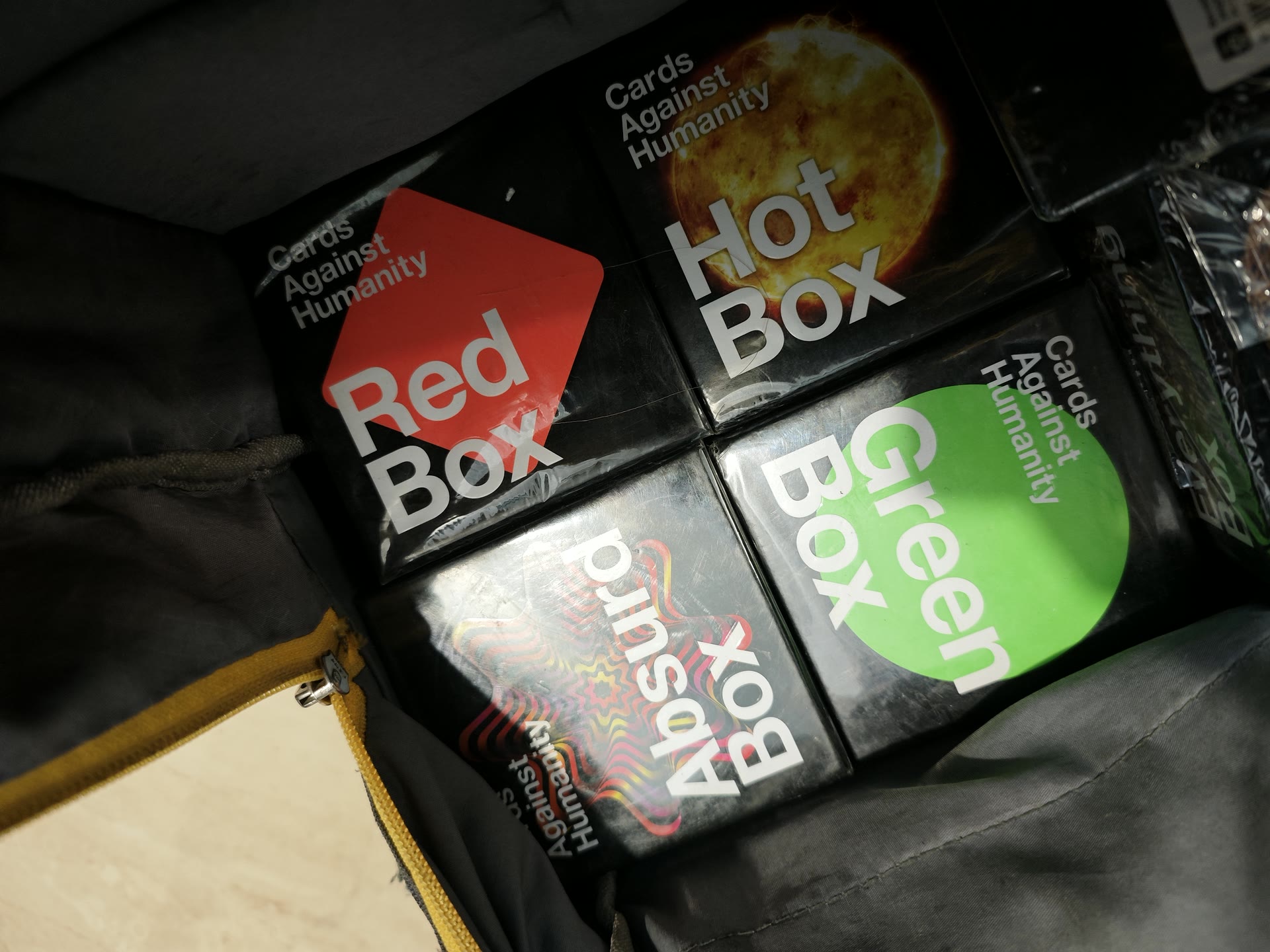 Close-up of unopened Cards Against Humanity expansion boxes arranged inside the small table beneath the television.