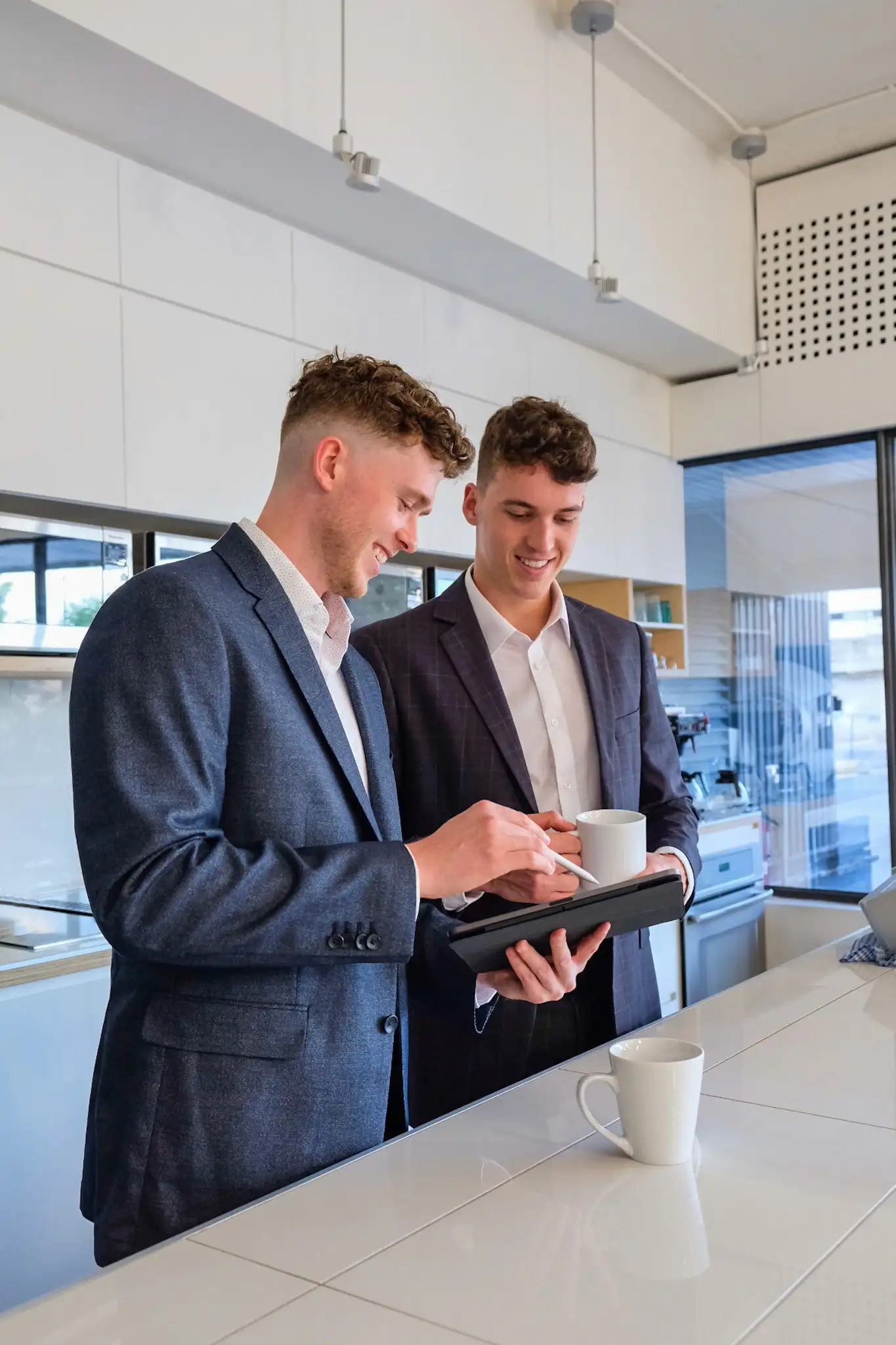 Les cofondateurs Olivier Roy (à droite) et Xavier Desbiens (à gauche) sourient en discutant autour d'une tablette tactile et d'un café dans la cuisine de l'entreprise.