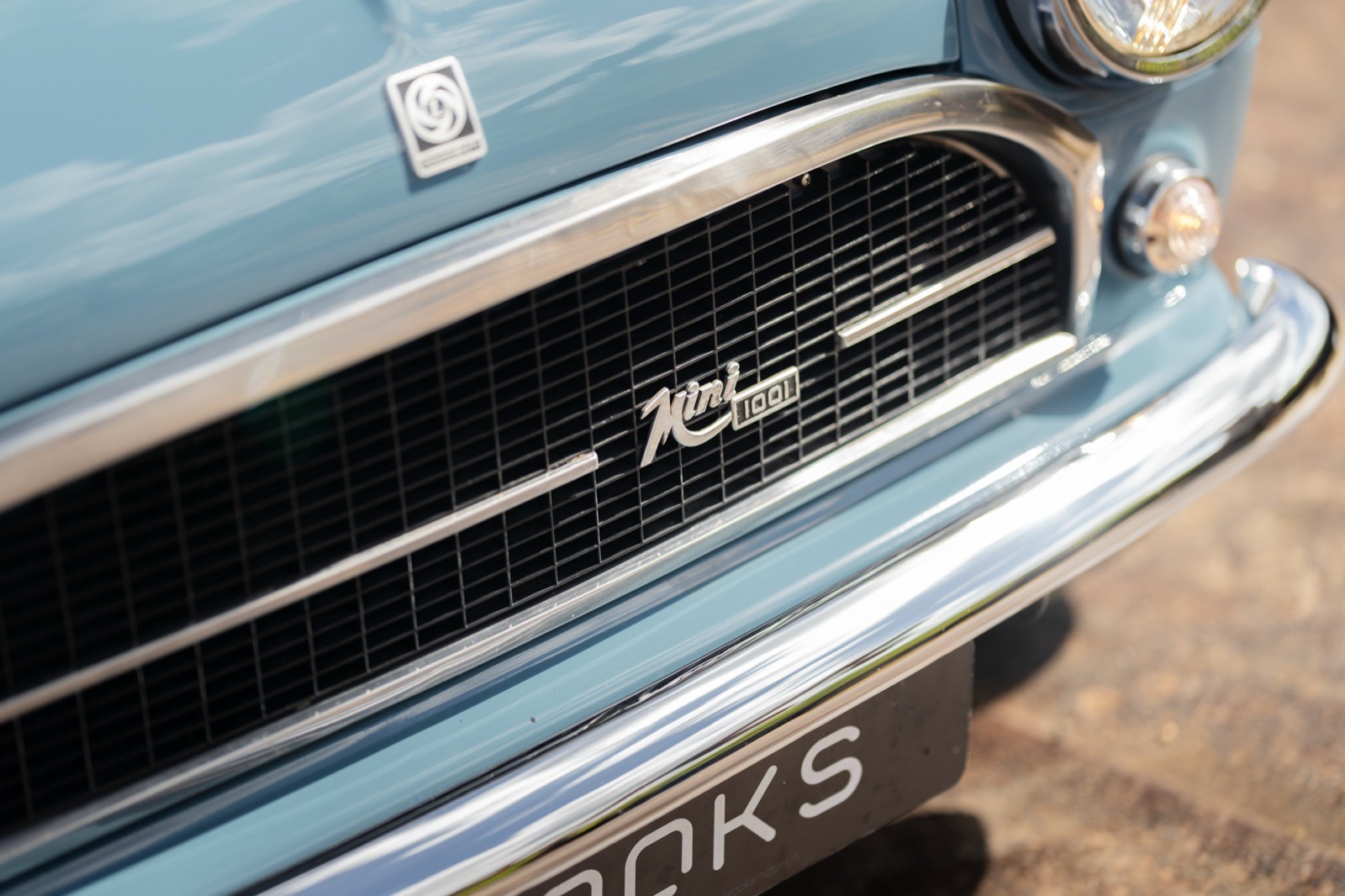 Close-up of a vintage car's front grille, featuring a chrome logo and a sleek blue exterior.