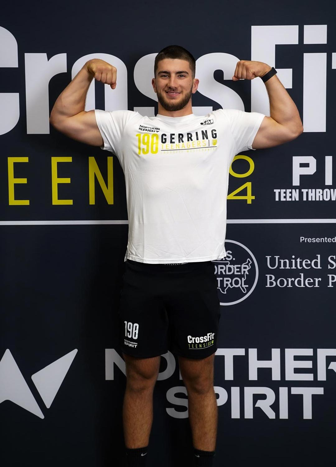 A dimly lit gym scene featuring a barbell rack and weights on the floor, with large windows in the background.
