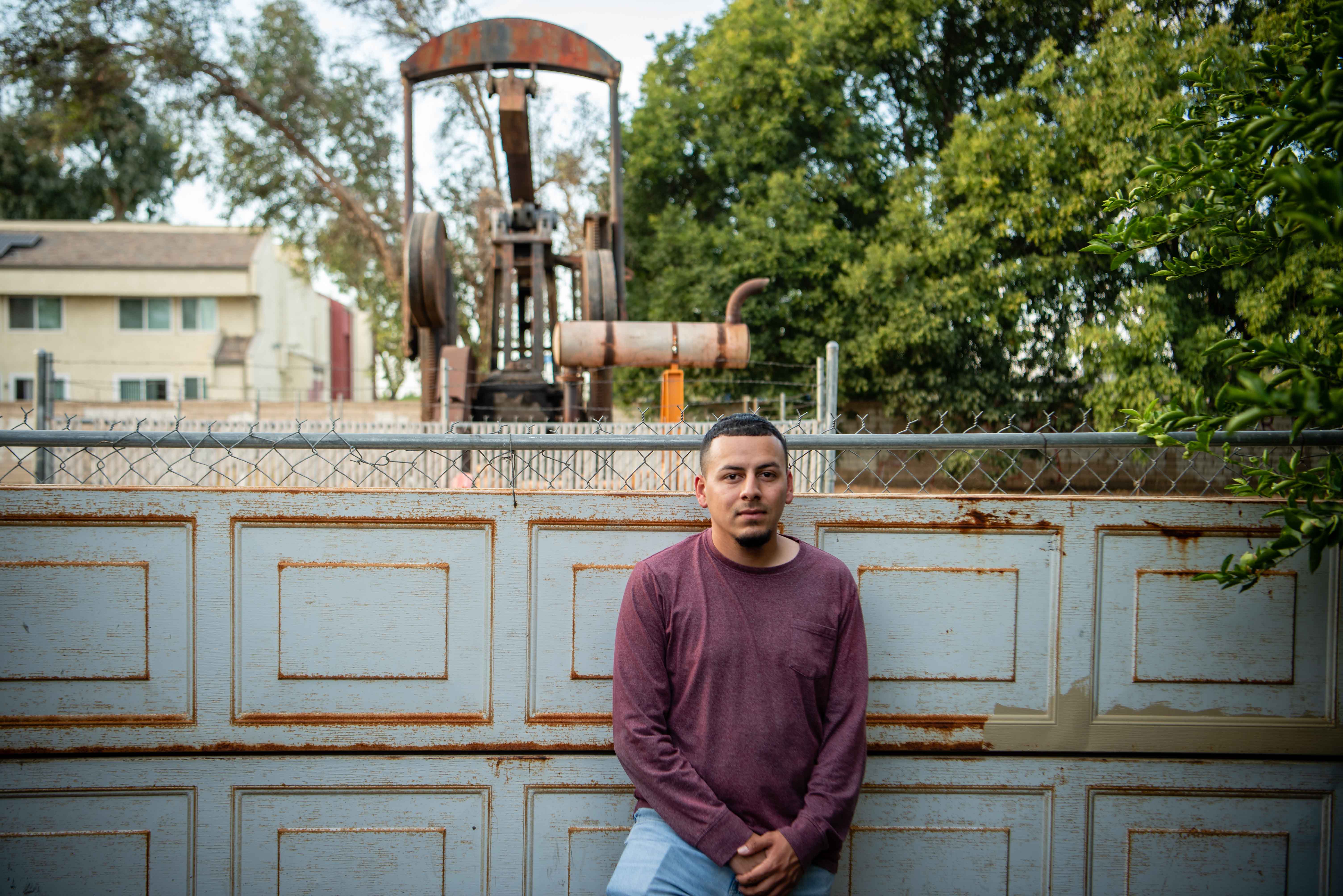 A man in front of an oil rig within a neighborhood in California.