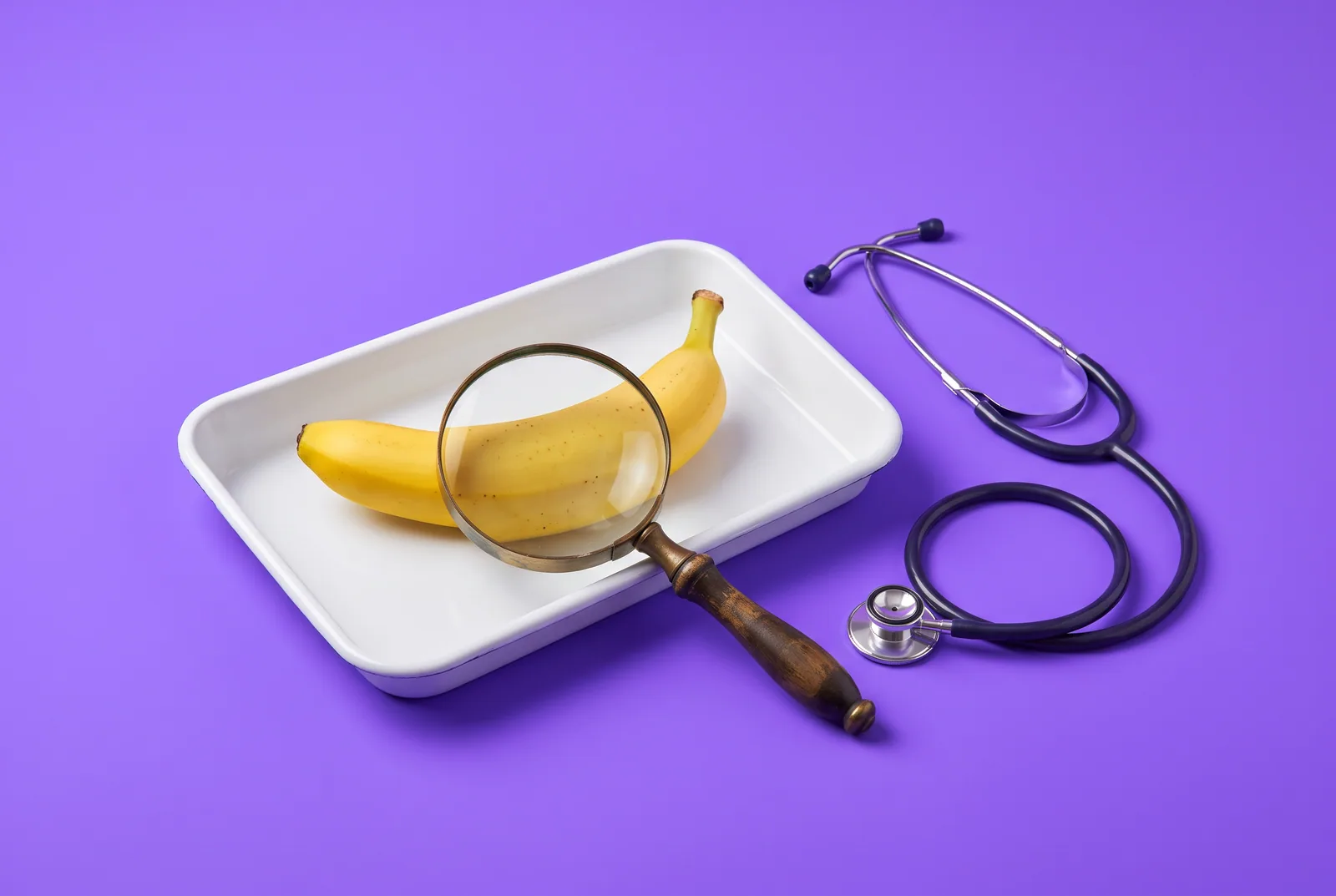 A banana under a vintage magnifying glass on a white tray beside a stethoscope, other causes of delayed ejaculation