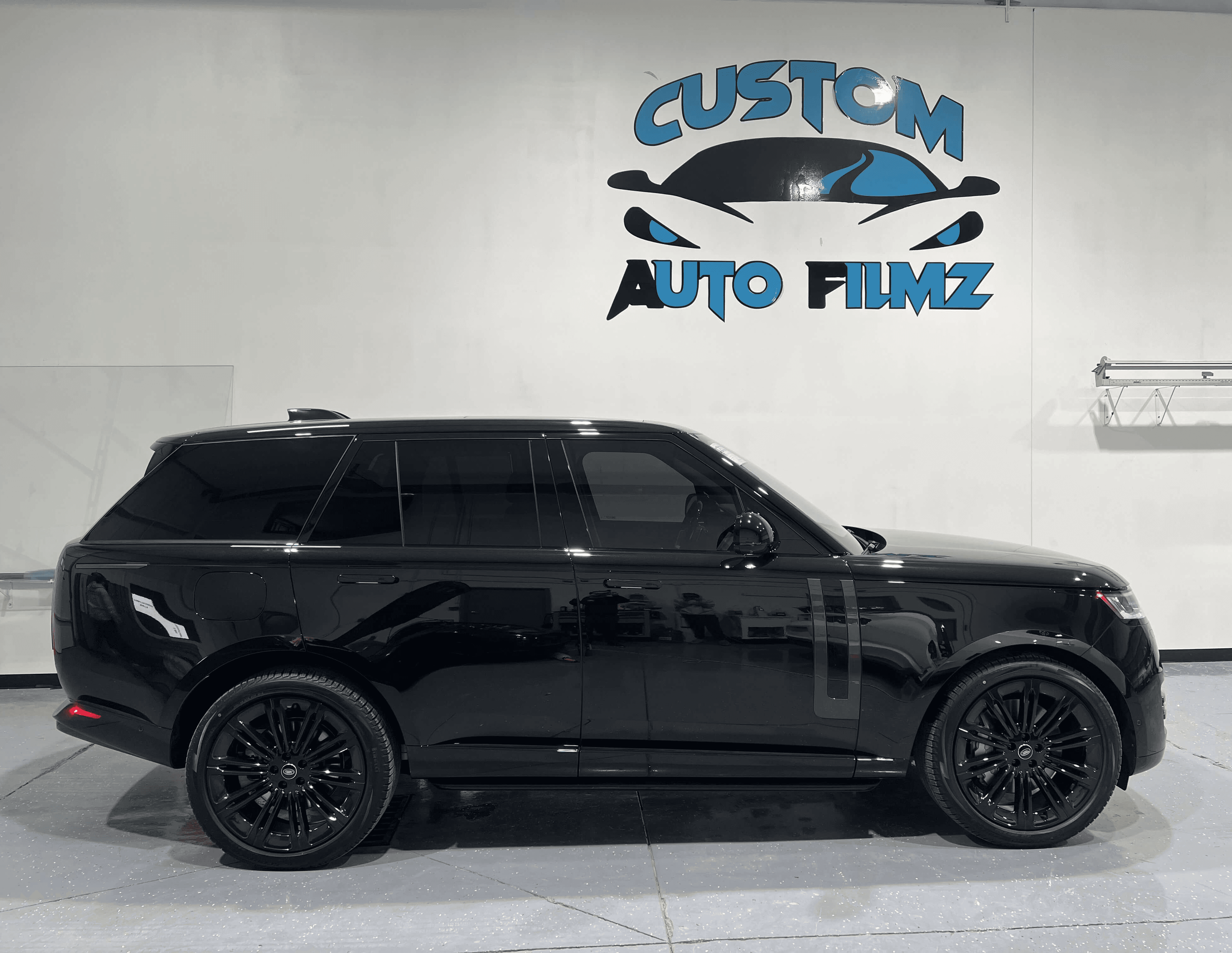 A glossy black Range Rover is parked indoors on a polished gray floor.