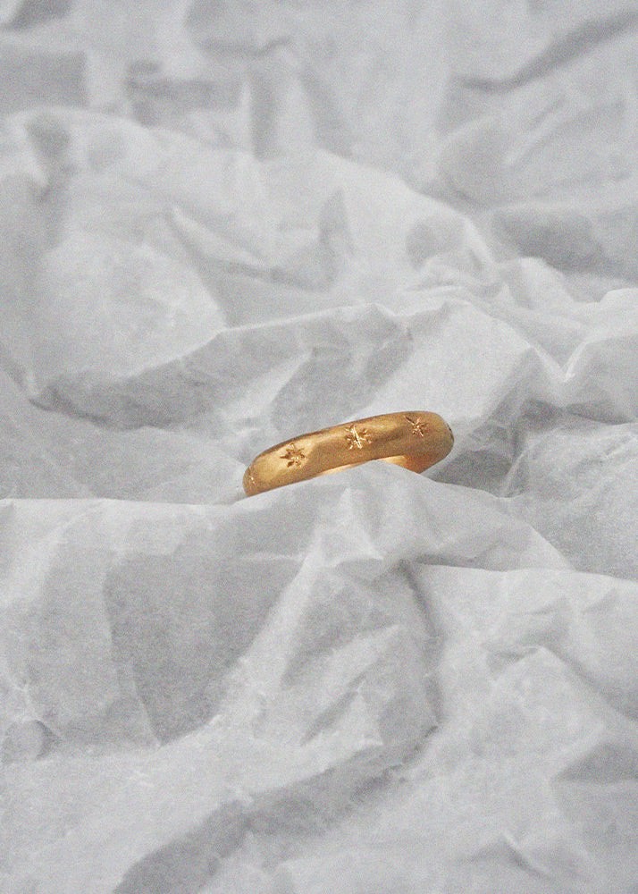 Gold ring with sparks engraved design on a textured white fabric background
