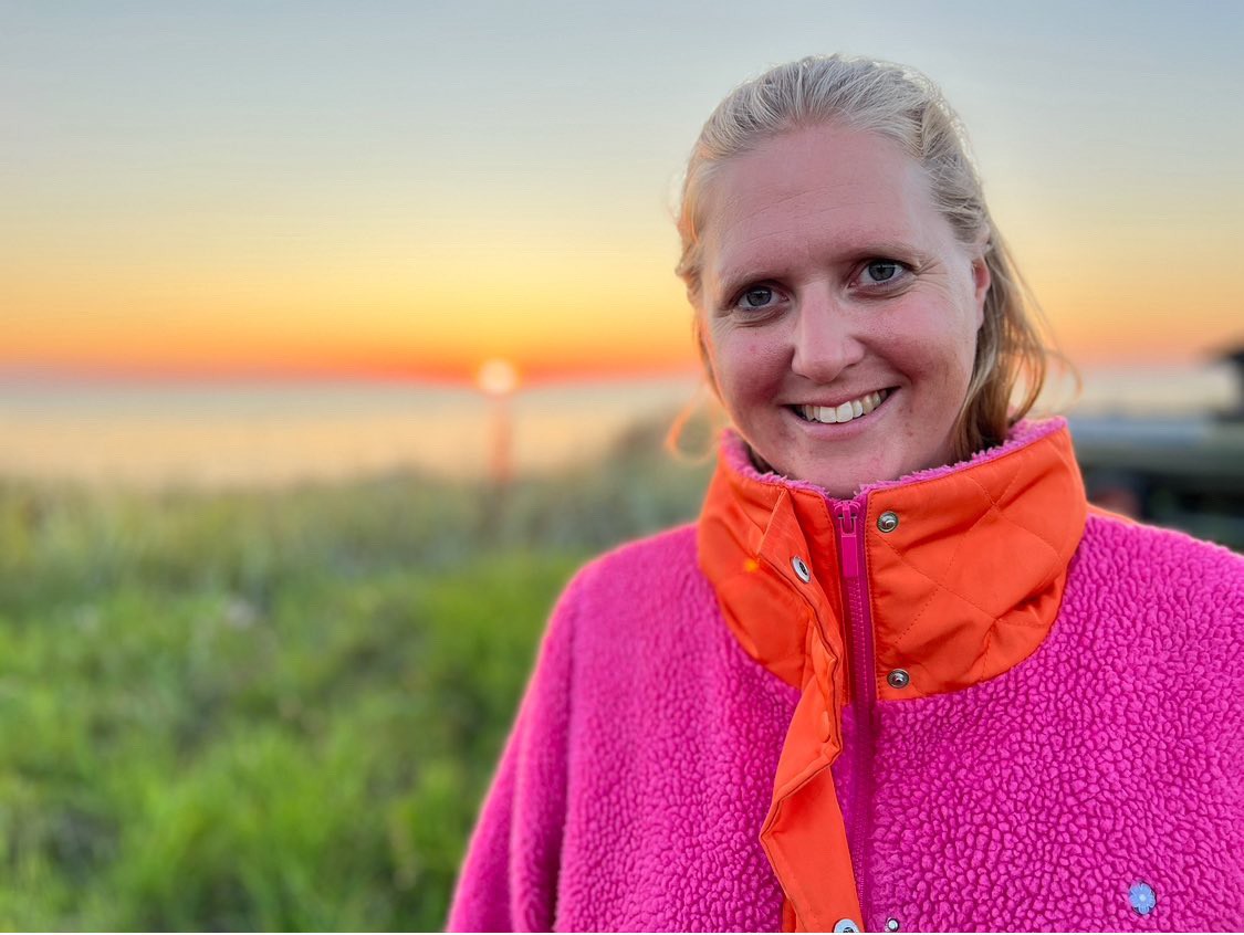 Clara utomhus i solnedgång framför ett fält, i rosa och orange fleecetröja