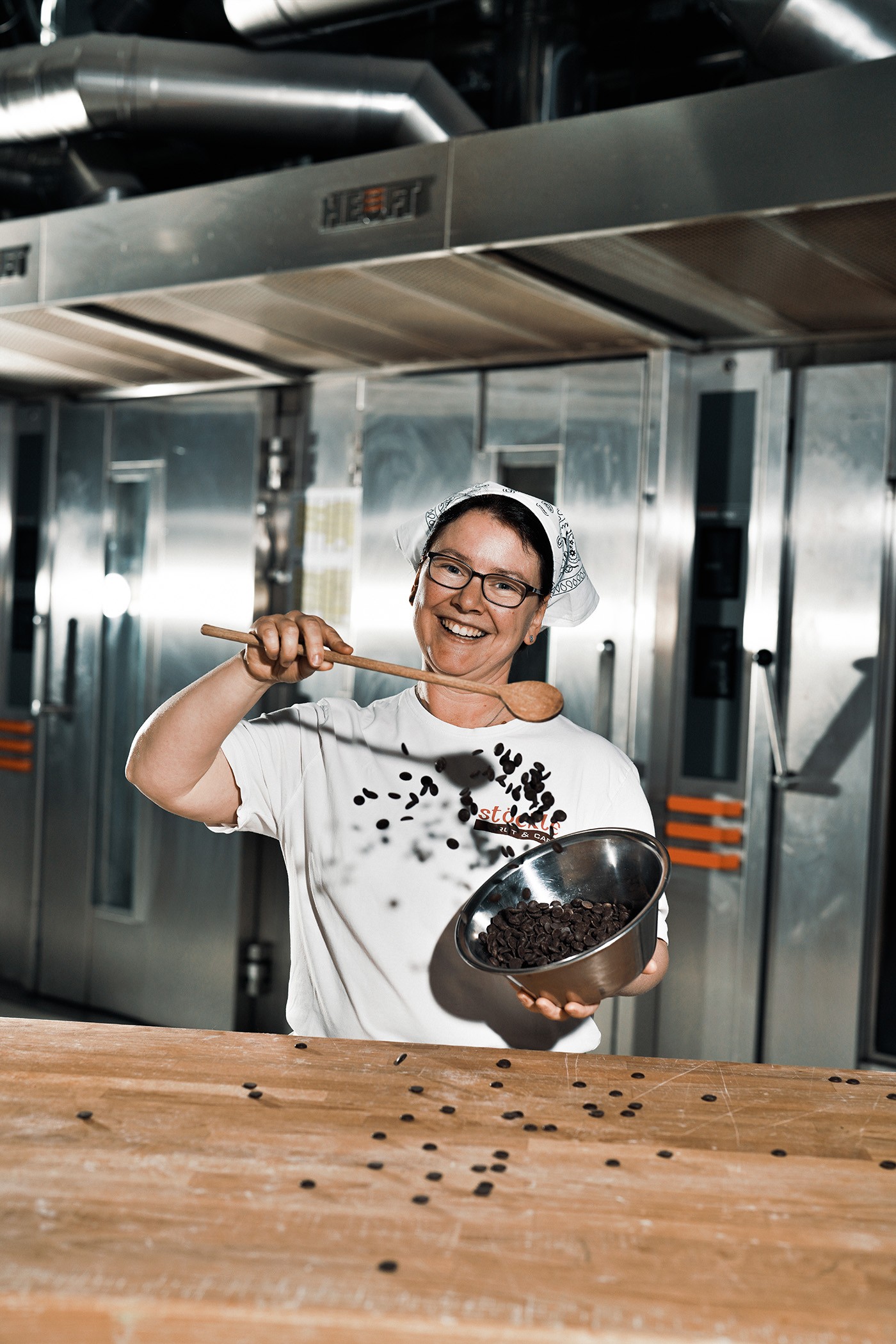 lächende Konditorin arbeitet mit Schokolade vor der Kamera, mit metallischen Türen im Hintergrund