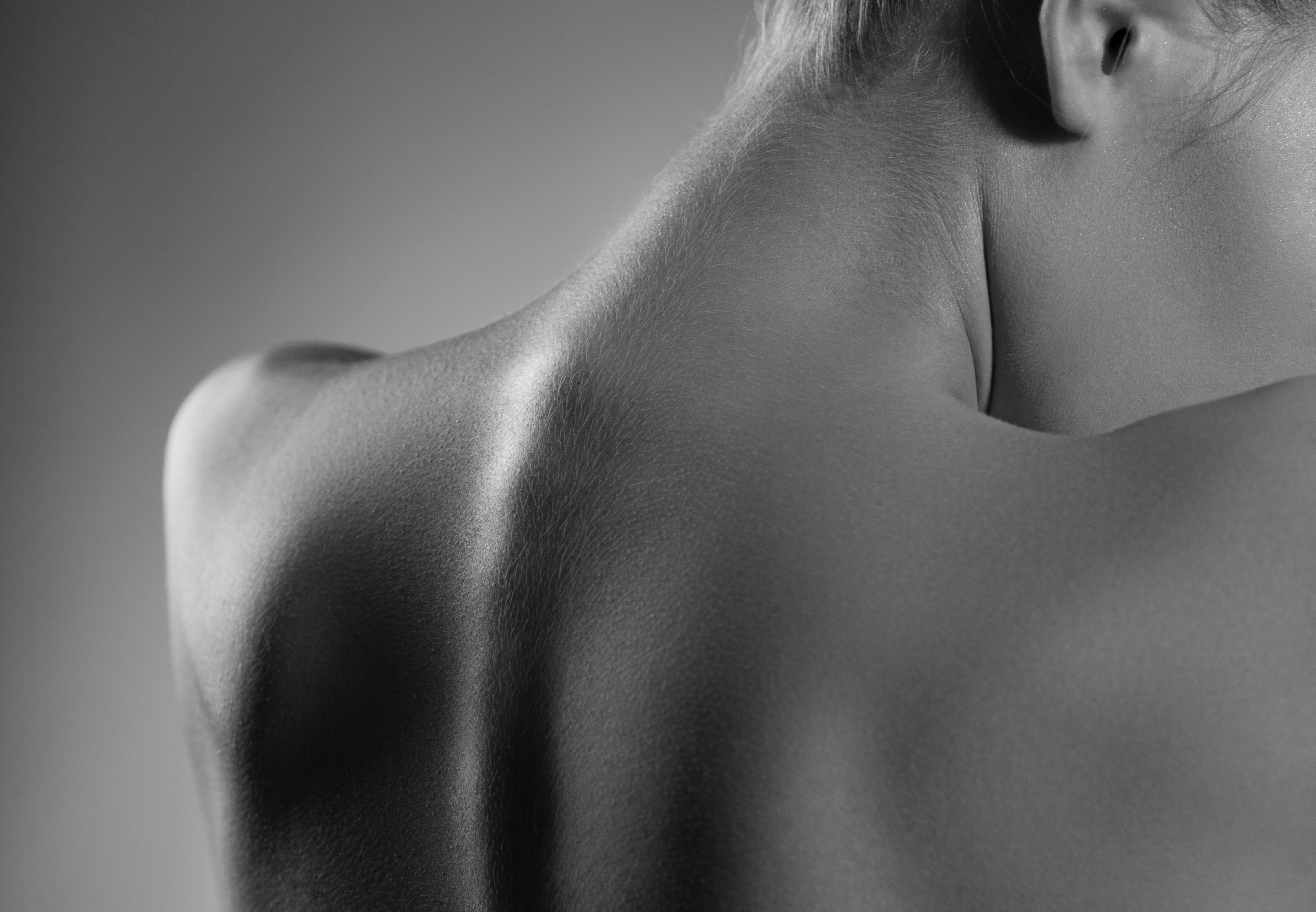 Schwarz-weiße Nahaufnahme eines nackten oberen Rückens und Nackens, der die Konturen von Wirbelsäule und Schultern betont.
