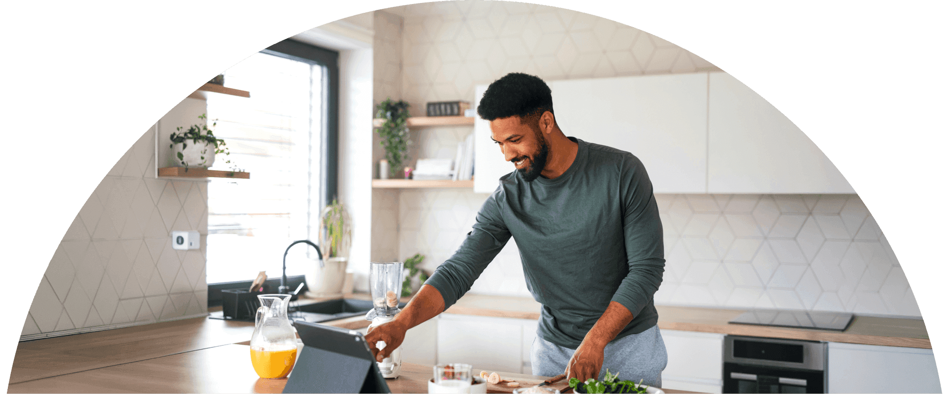 Man smiles while preparing food in a bright modern kitchen and interacts with a tablet on the counter