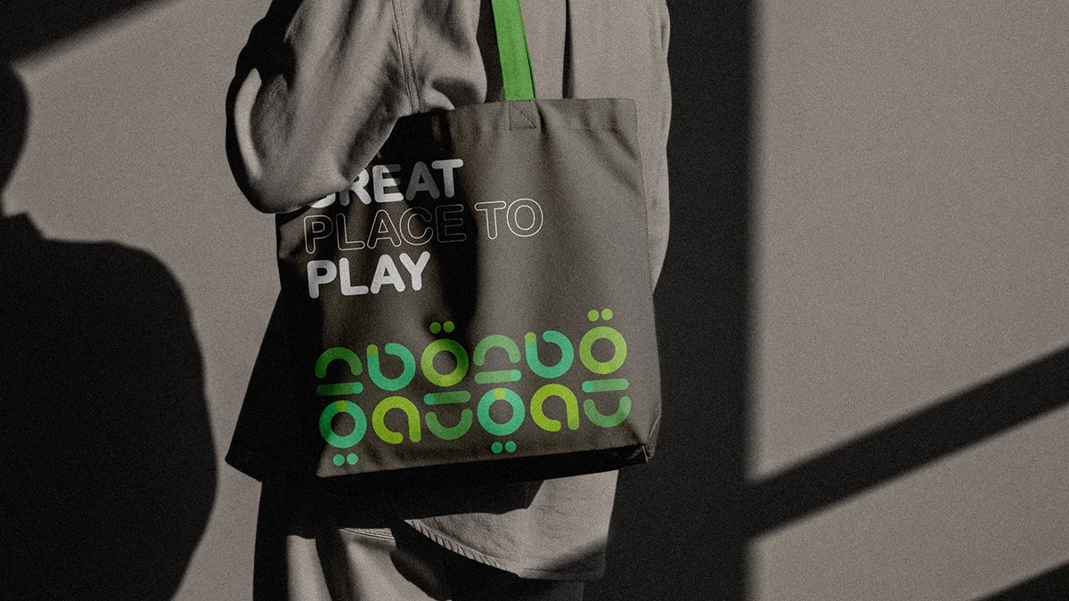 Person carrying a Hadayeq Dubai branded tote bag in a public park.