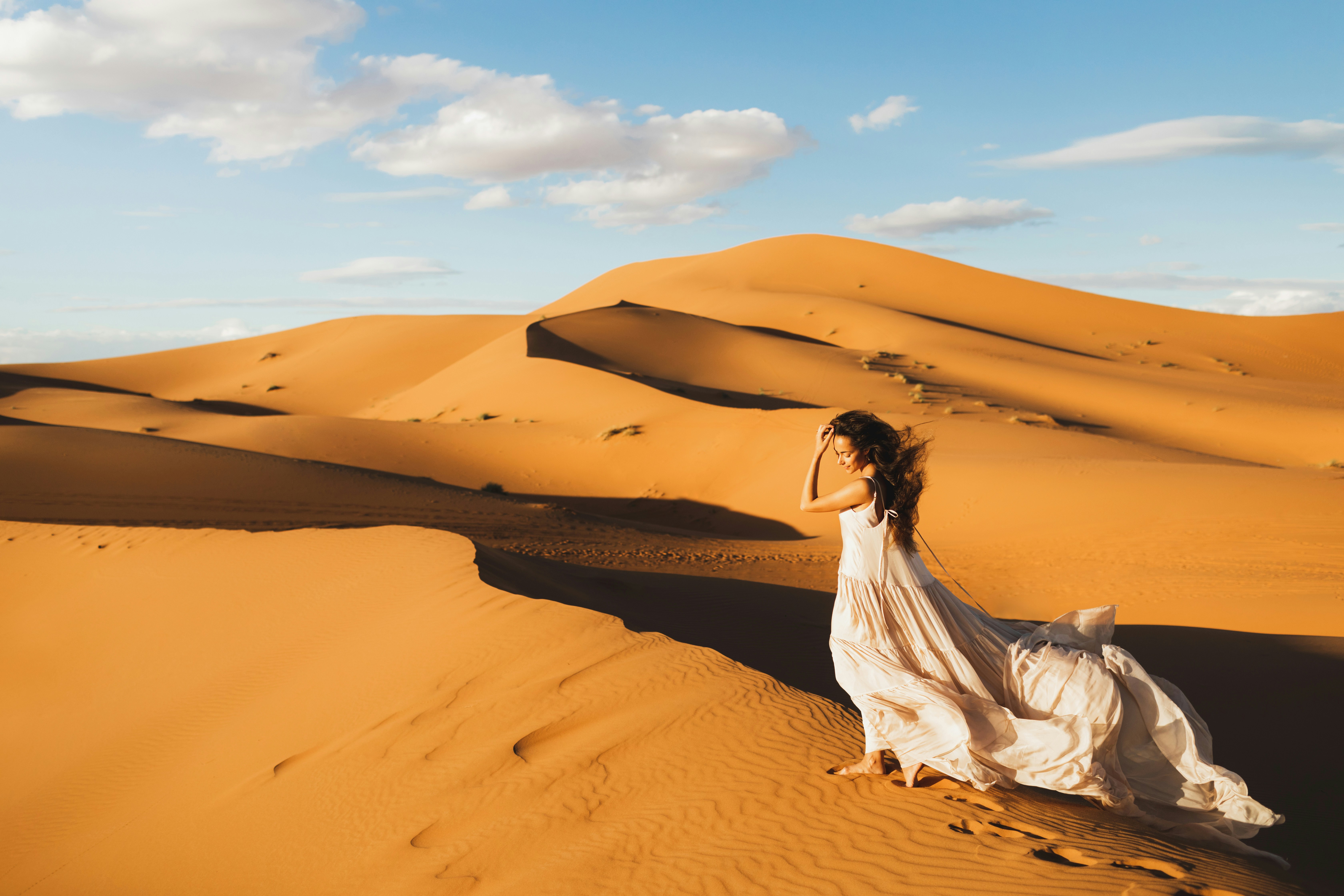 A serene desert landscape with rolling sand dunes under a cloudy blue sky.