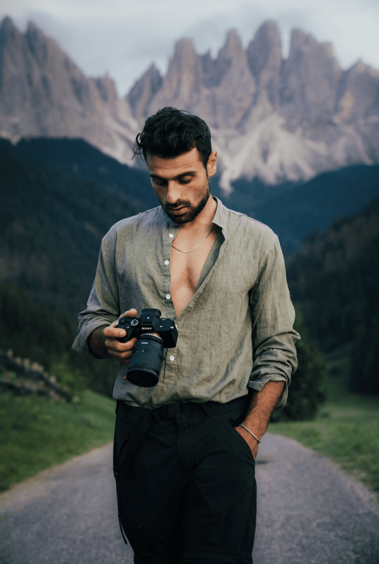 A smiling man with wavy hair and a beard, wearing a green jacket over a black shirt. He stands against a deep red background, conveying a warm, friendly tone.