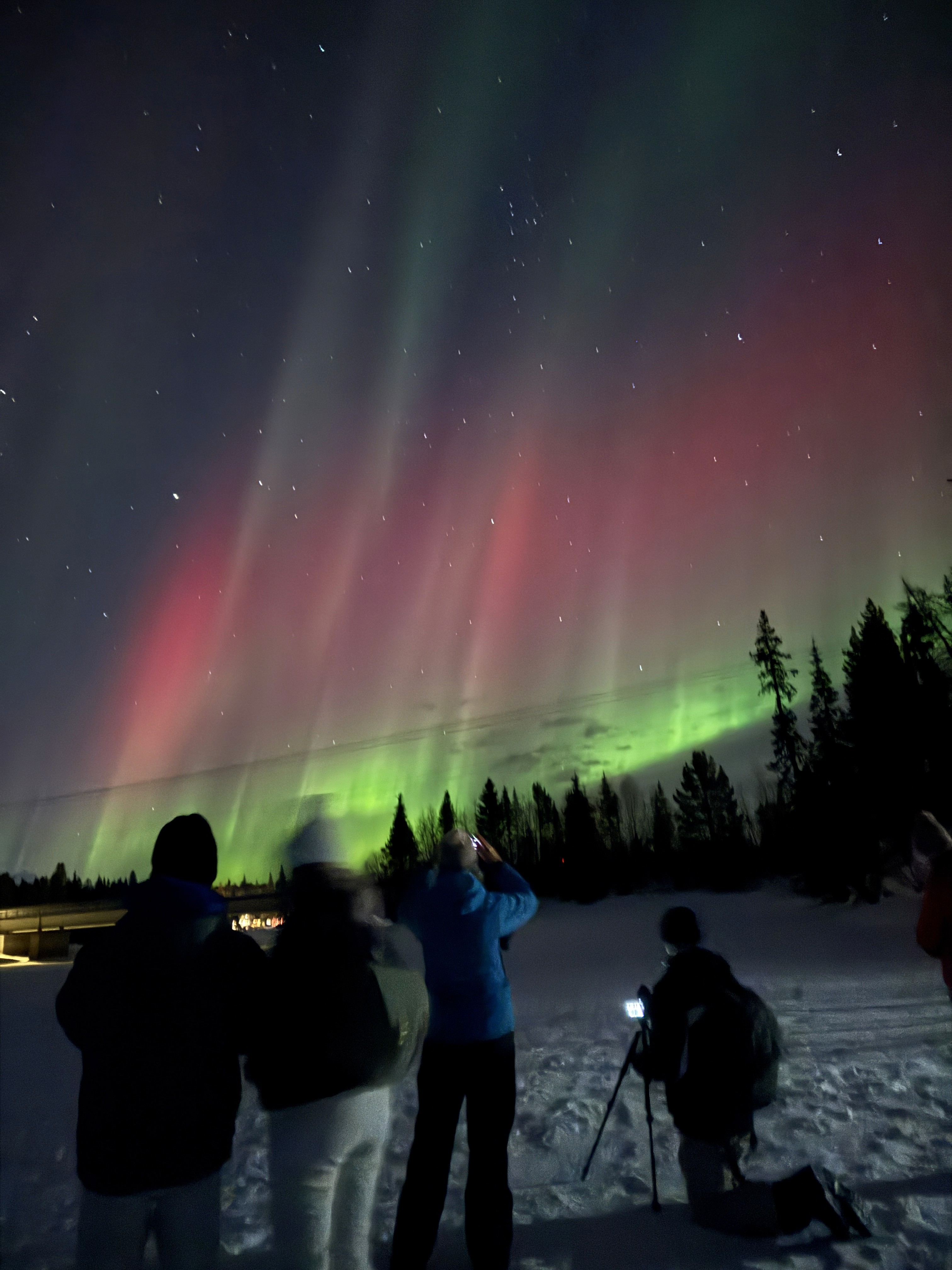 Northern lights above travelers in a snowy Arctic landscape