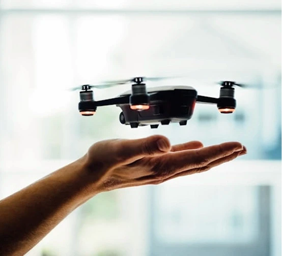 A small drone hovers above an outstretched hand indoors, showcasing deep tech and consumer innovation.