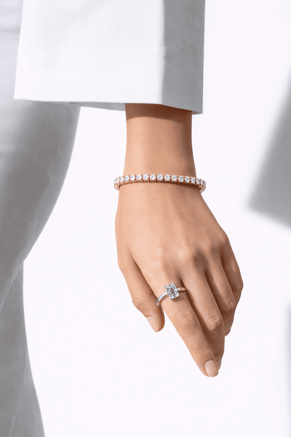 A woman's hand elegantly displays a sparkling diamond bracelet and a large, radiant diamond ring, set against a crisp white shirt for a sophisticated and luxurious look.