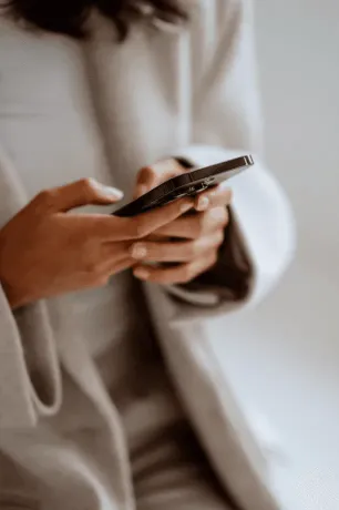 Young woman with short, dark hair and a yellow sweater looks serious, surrounded by hands holding smartphones, conveying intrusion and tension.