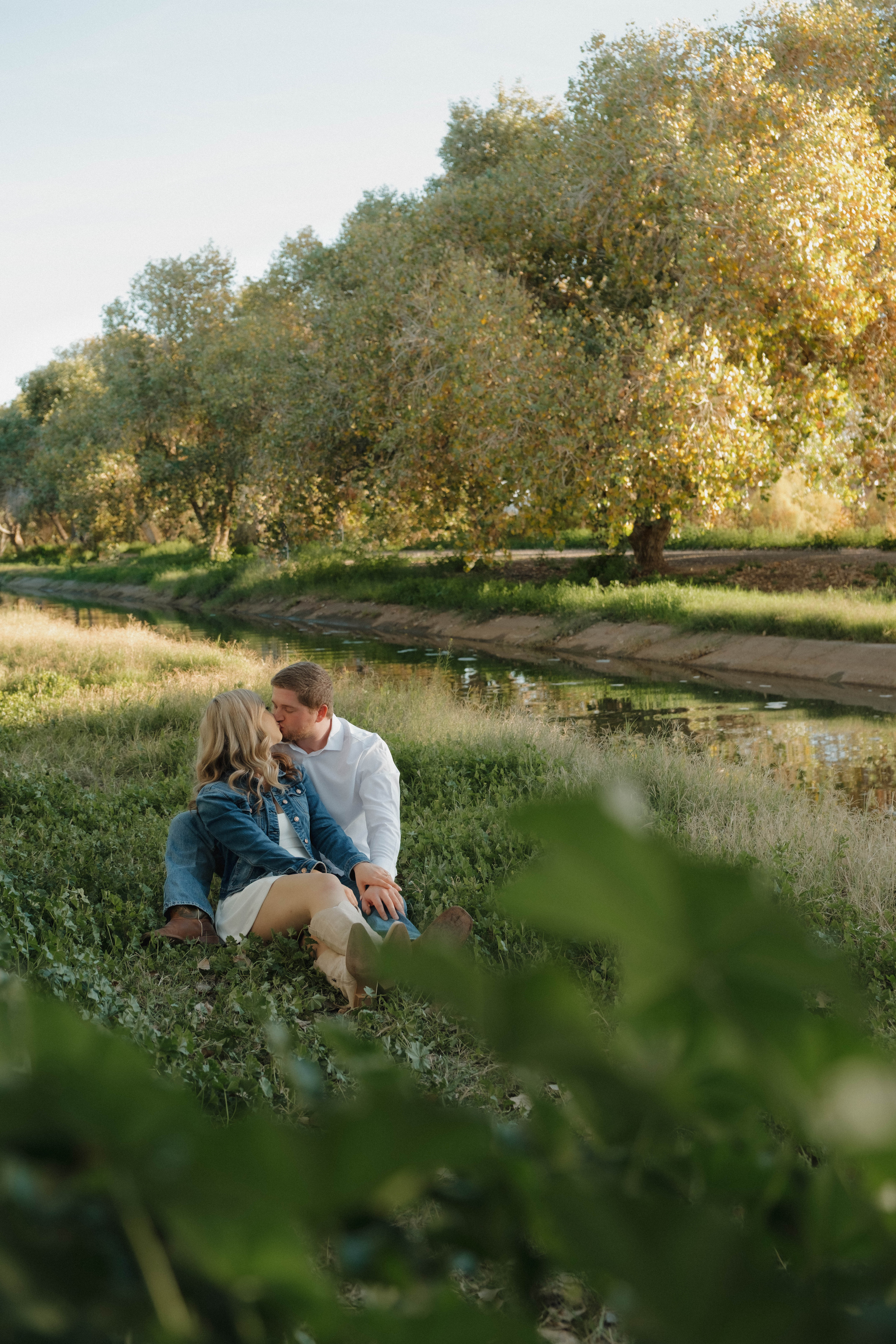 Outdoor maternity photography in Salt River, Arizona with a woman in a white crocheted top dress standing by the water.