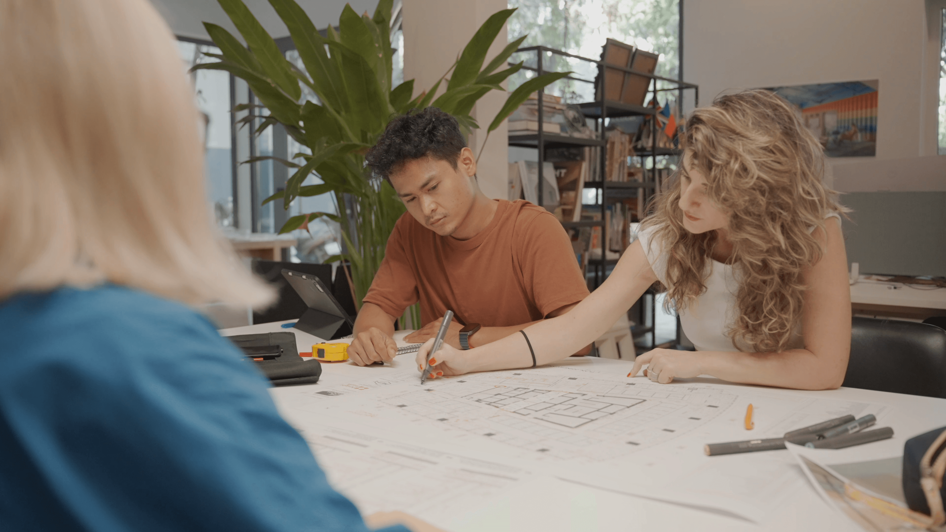Three professionals reviewing architectural floor plans and drawings at a table during an early-stage design consultation, representing the briefing and planning work that precedes design decisions on a commercial project
