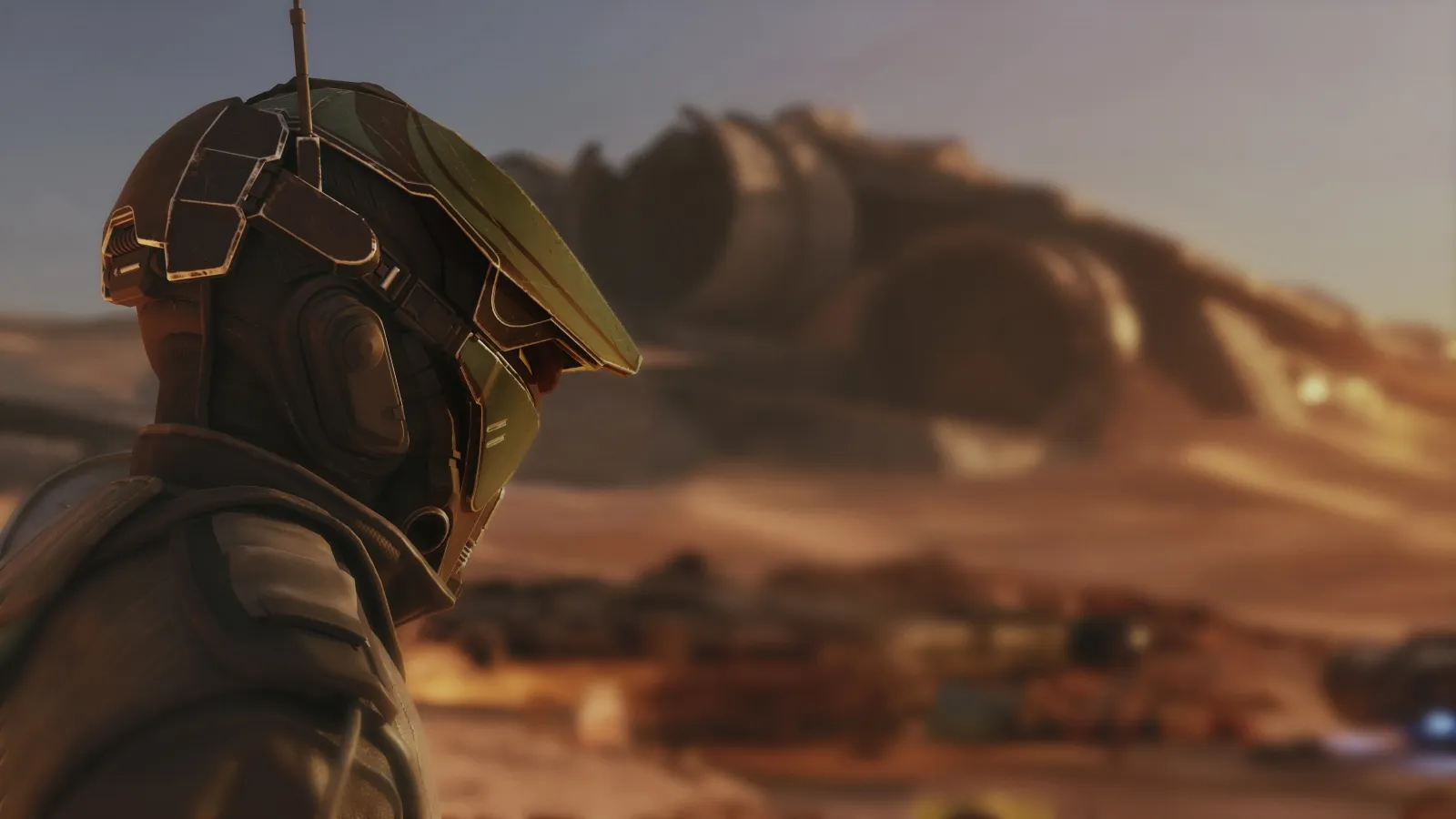 A futuristic character in advanced armour gazes across a barren desert landscape with large, partially buried, domed structures in the background, suggesting an alien or post-apocalyptic setting.