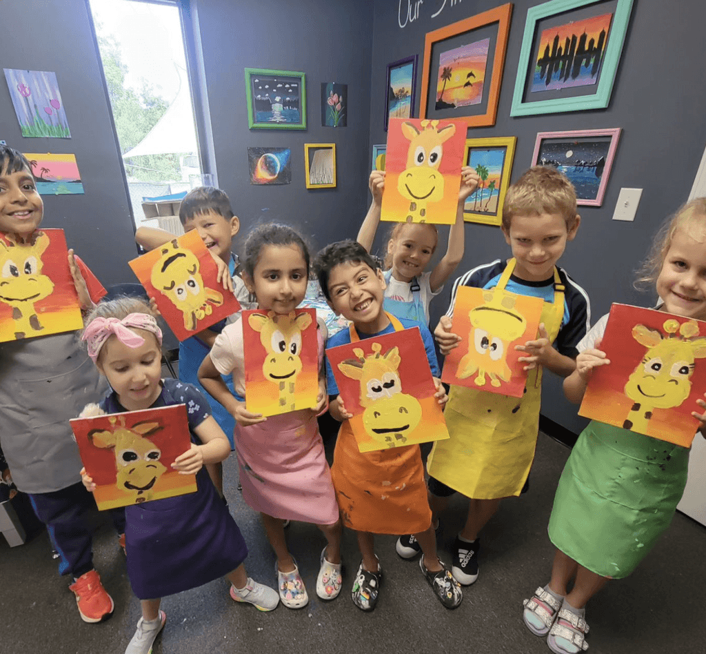 SportPlus art class students posing with warm compositions they painted of giraffes