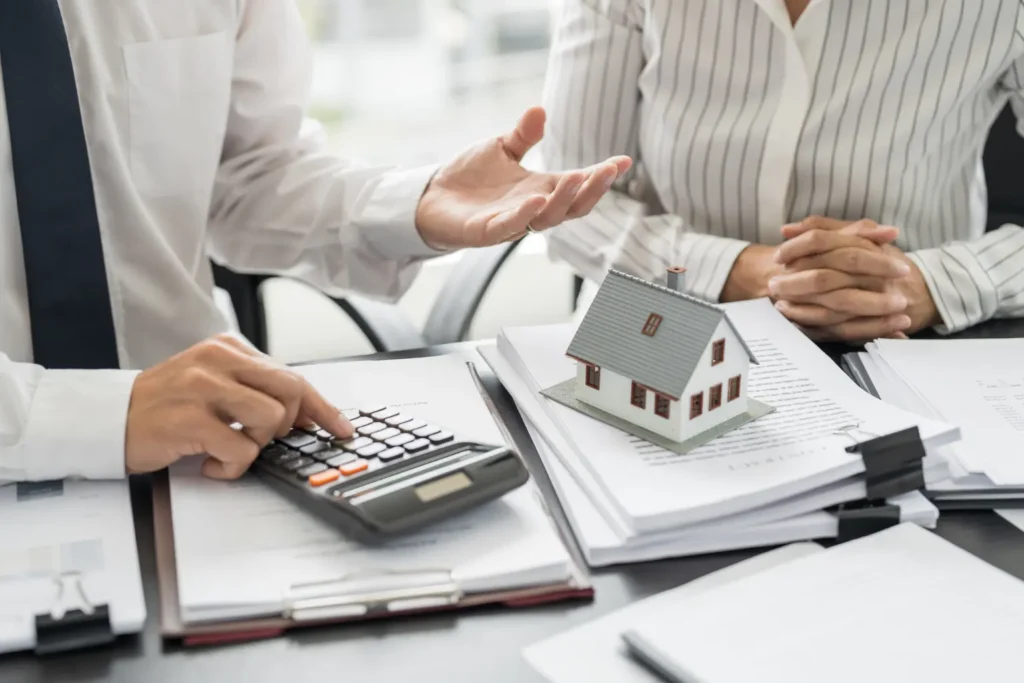 rental property management agent discussing costs with calculator and house model on paperwork