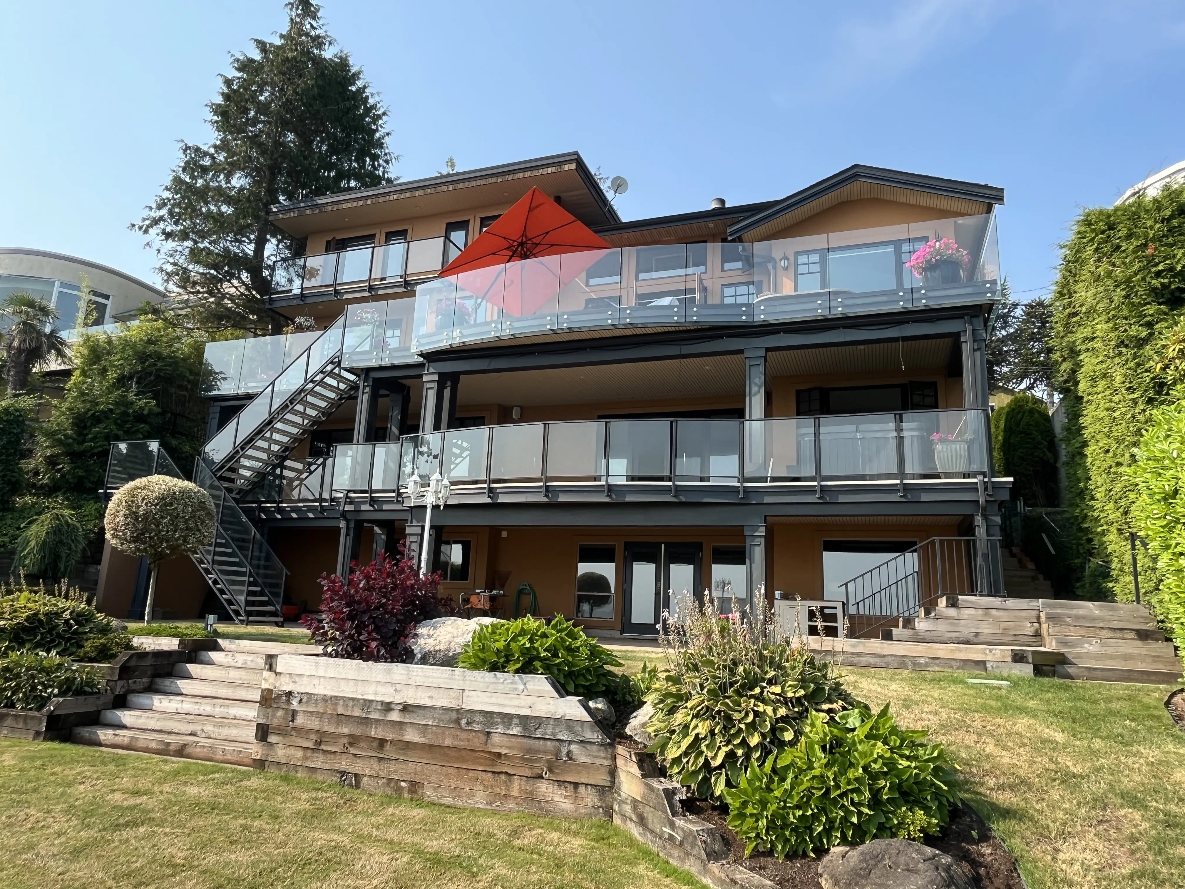 Three storey Vancouver Island home with glass railings on stacked balconies and an exterior glass railed staircase