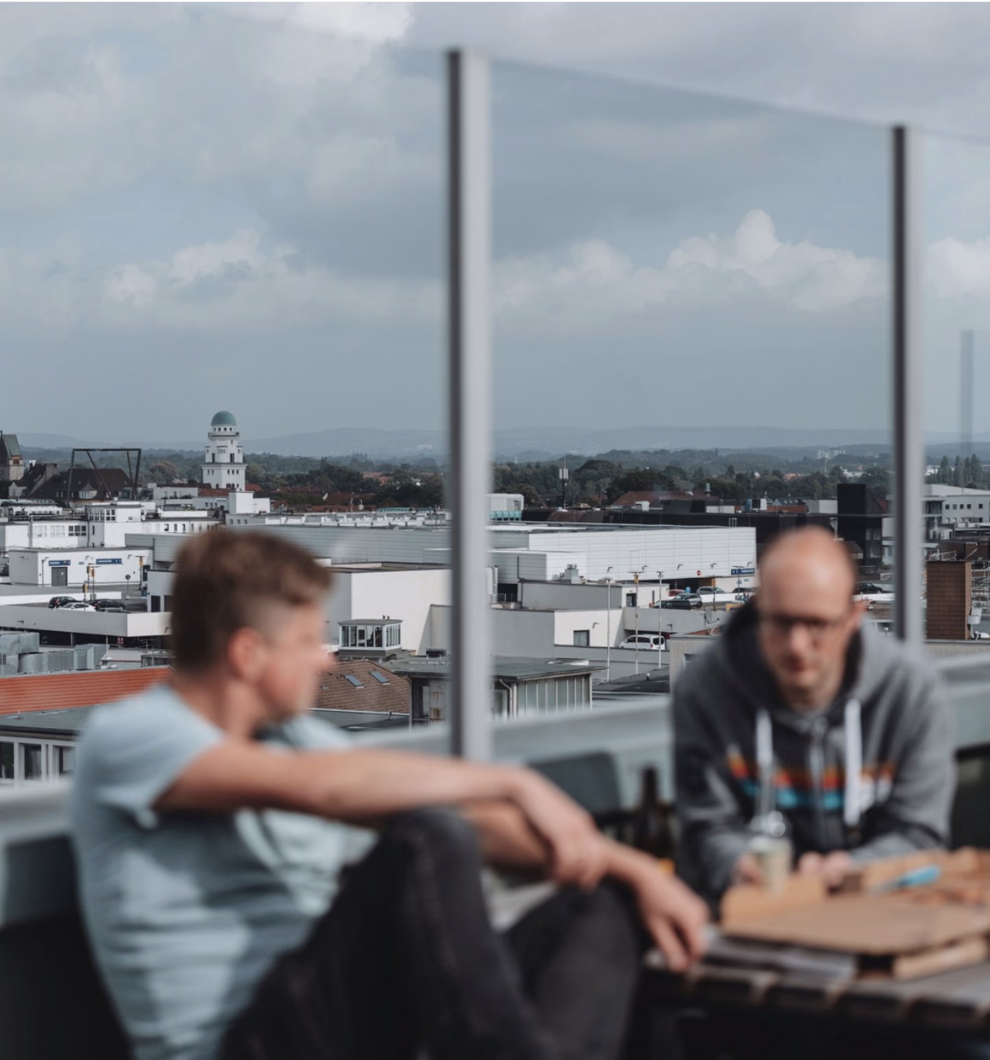 Zwei Personen im Gespräch auf einer Dachterrasse mit Stadtblick – steht für offene Zusammenarbeit und Austausch im mercury.ai Team