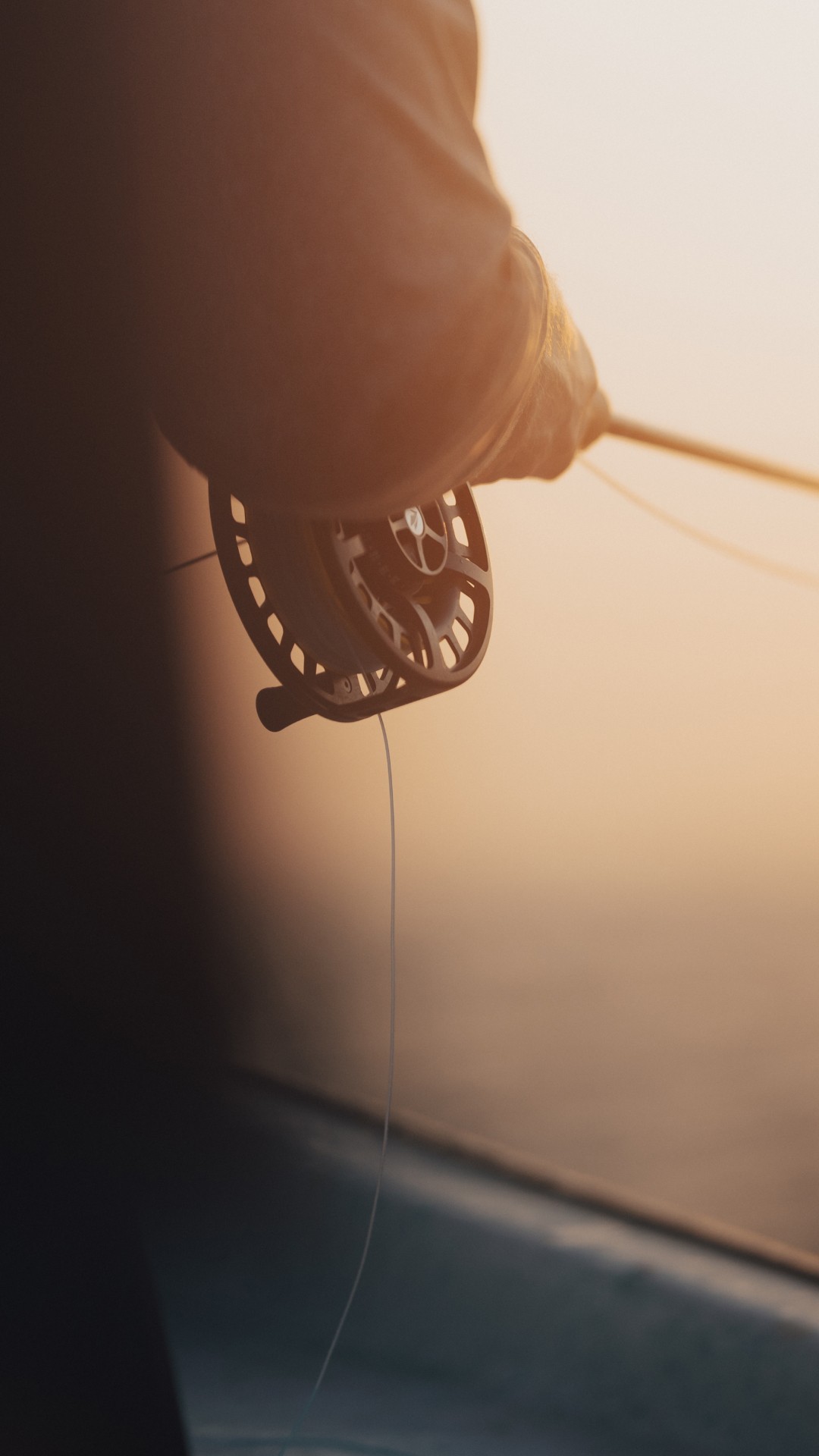 Closeup of a person holding a fly fishing rod and reel in glowing warm sunlight