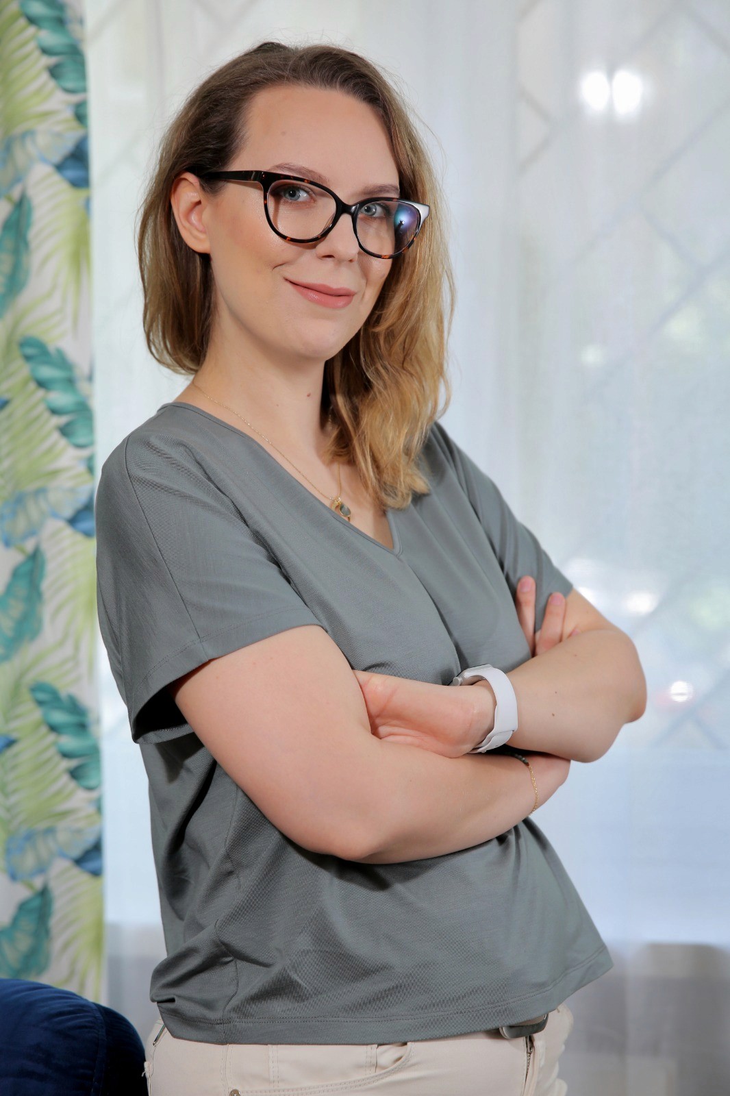 Smiling female therapist with short gray hair, wearing a brown top and a purple shawl, surrounded by a cozy background.