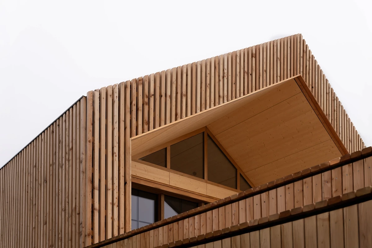 Auskragendes Dach über der Loggia mit Eckfenster, gerahmt von senkrechten Holzlatten