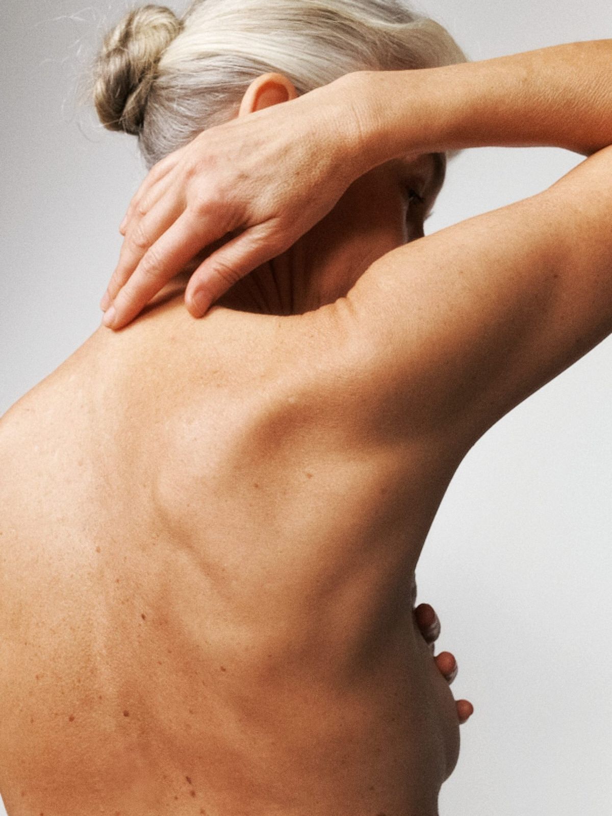 THe back of a woman who is reaching behind her to tough the bottom of her neck