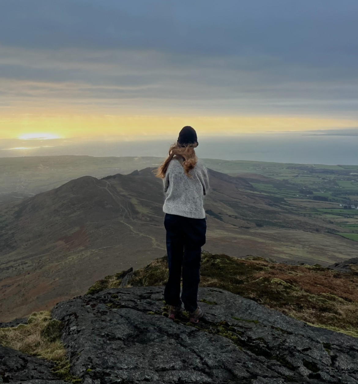 A smiling young man with crossed arms, wearing a plaid shirt and white t-shirt, poses against a dark background.