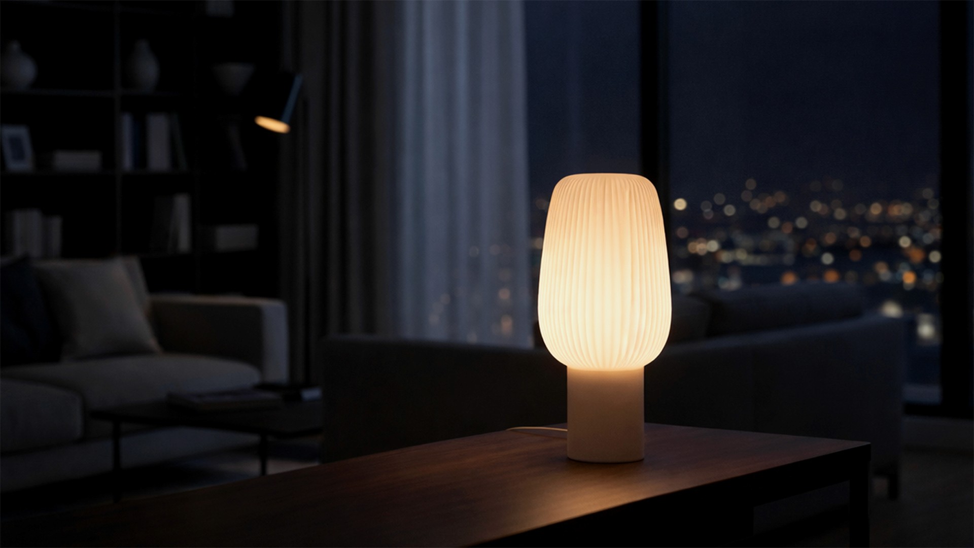A glowing, modern table lamp with a ribbed shade sits on a dark table against a blurred night city skyline.