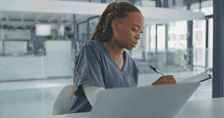 Healthcare worker writing notes on a clipboard in a modern clinical setting.