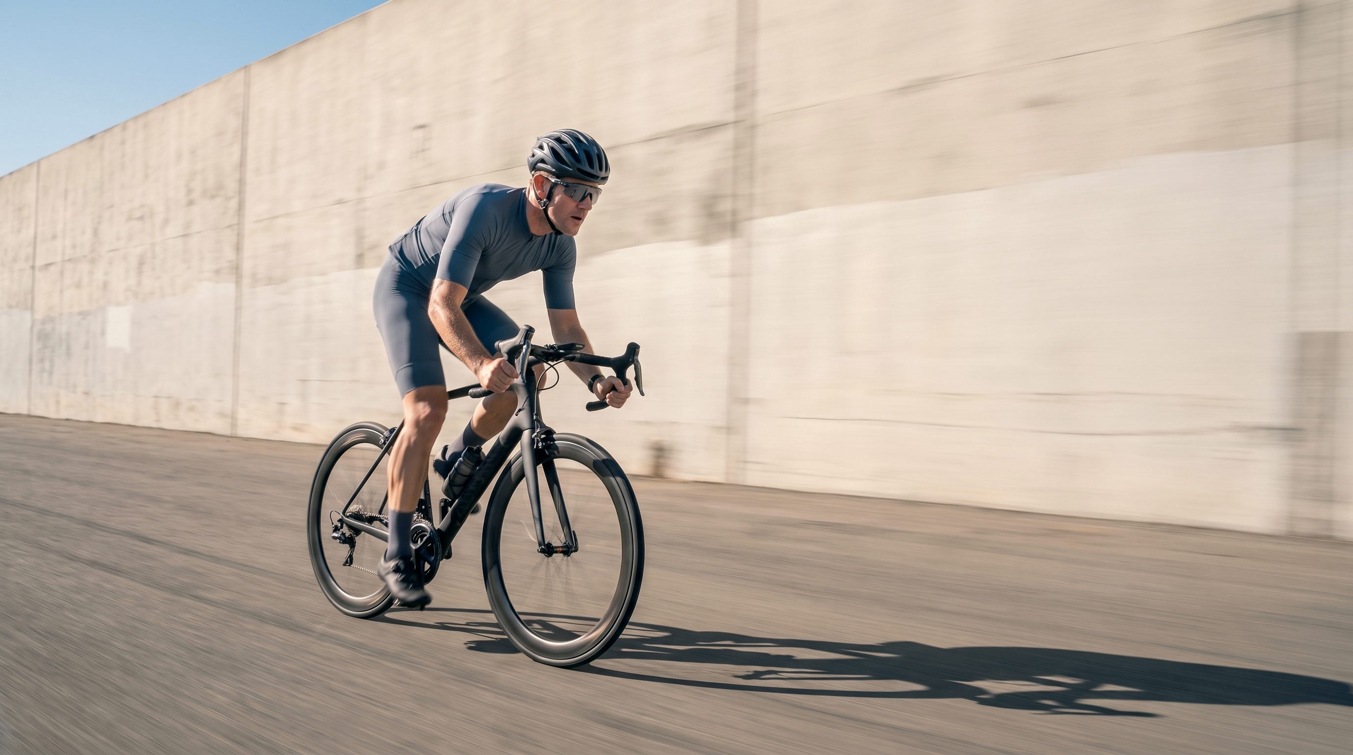 Radfahrer fährt bei Hitze an einer hellen Betonwand vorbei