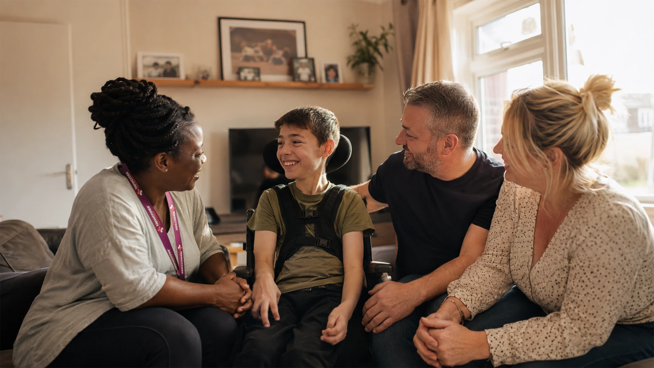 Support worker sharing a warm moment with a young adult wheelchair user and his family during a home visit.