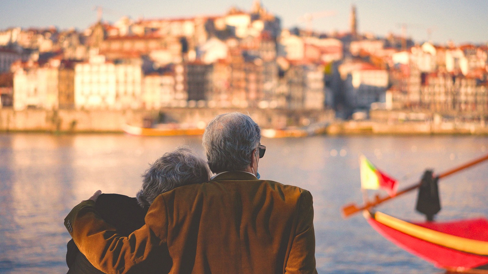 An older couple overlooking a riverside city at sunset, reflecting shared values, connection, and multigenerational travel experiences in Portugal.
