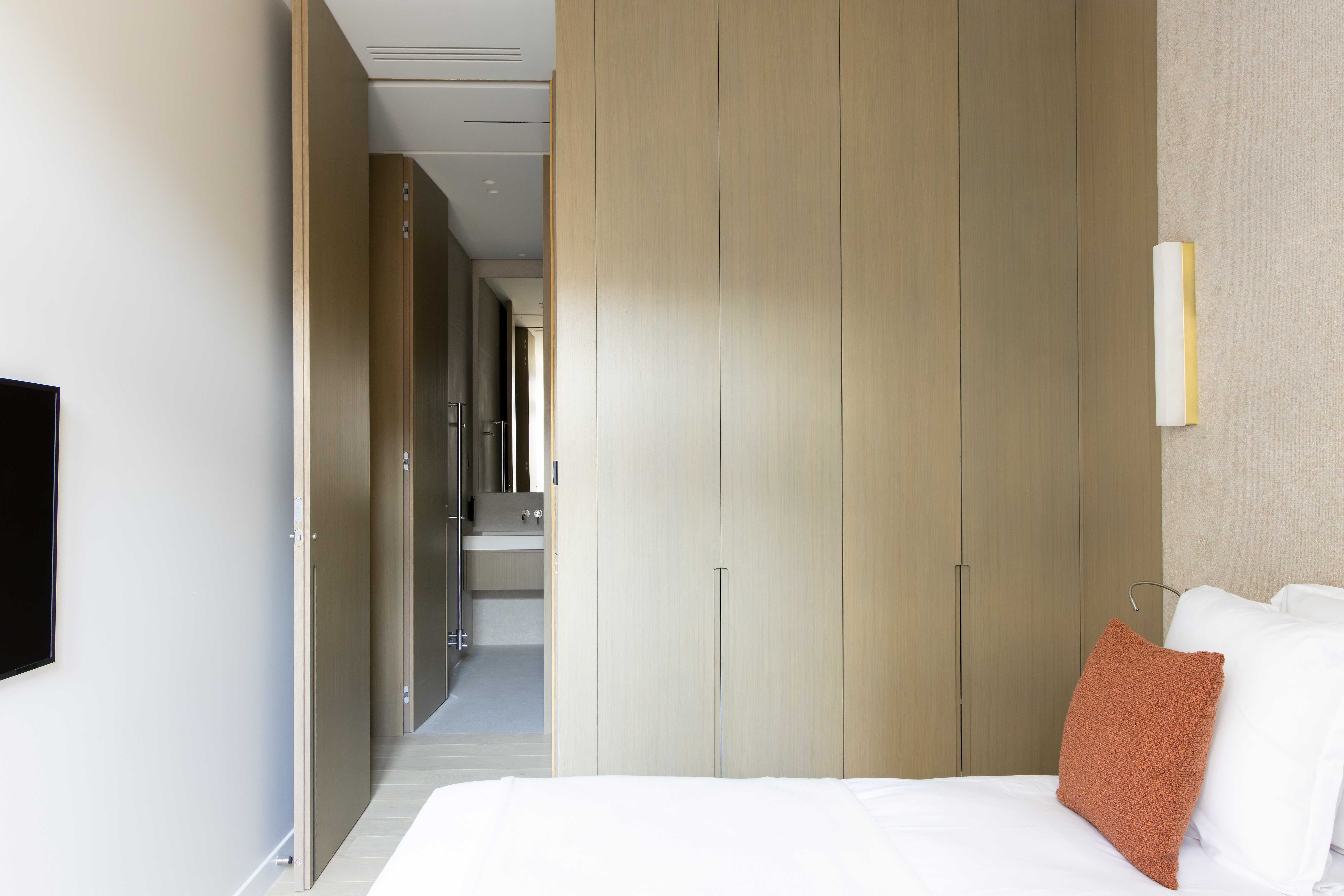 Chambre avec grands placards en bois clair, passage vers salle de bains, coussin terracotta et applique doree