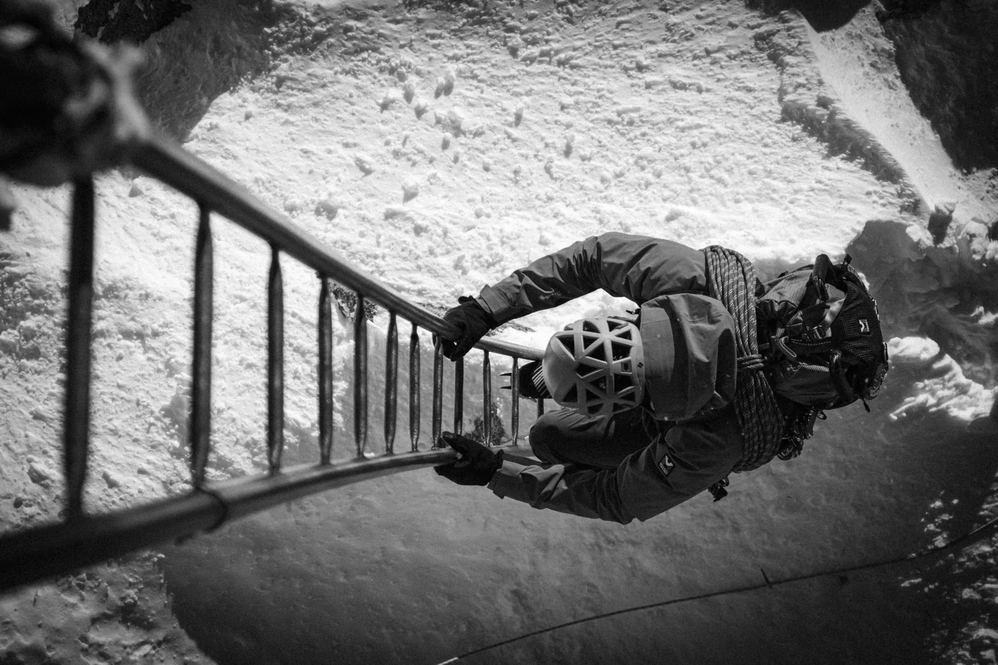 Alpiniste traversant une échelle sur glacier, scène en noir et blanc, équipement Millet.