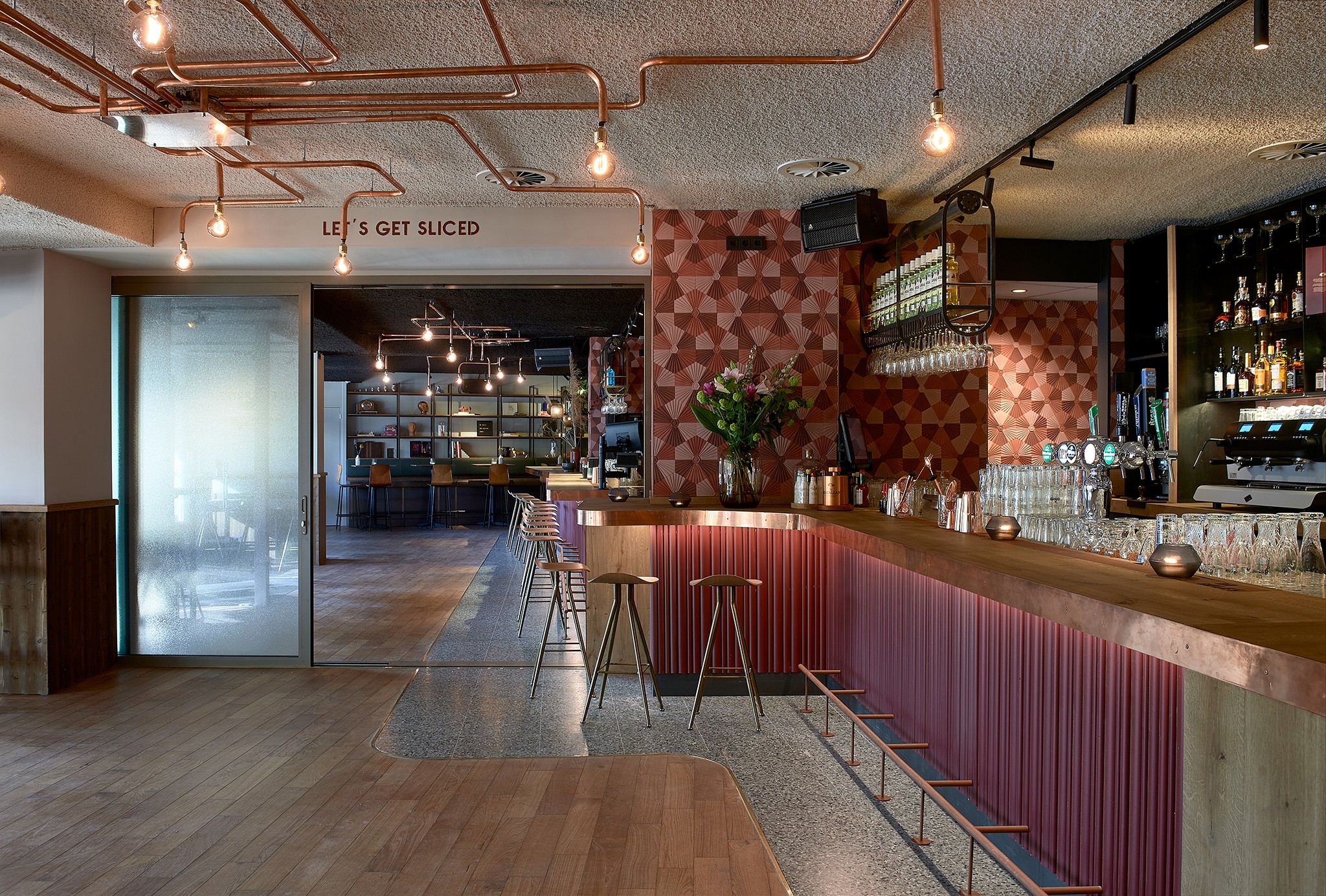 Interieur bar met koperen buizen aan het plafond en houten bar met krukken.
