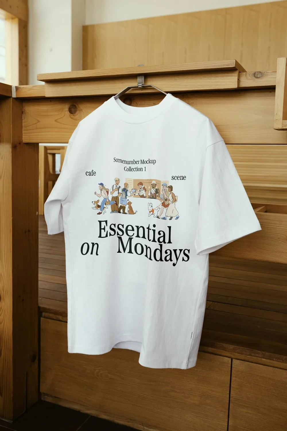 A light blue t-shirt mockup featuring vibrant text and illustrated graphics, displayed on a hanger against a wooden interior backdrop with warm natural lighting.