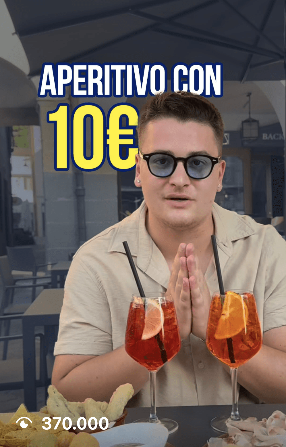 A smiling couple takes a selfie under a clear blue sky. The woman wears a red jacket, and the man, in a green top, holds a smartphone.