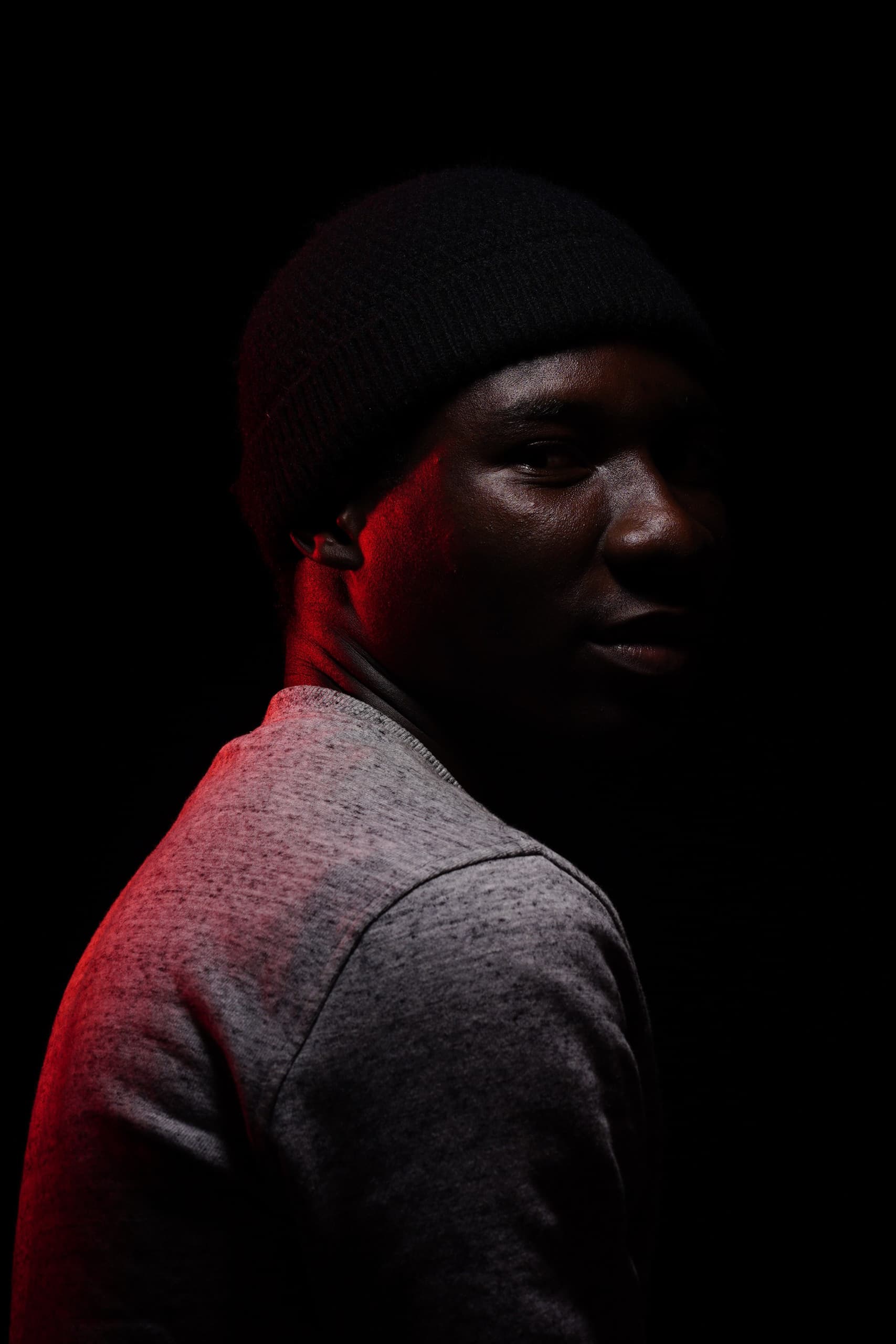 Person wearing a blue puffer jacket and red backpack standing in front of a light blue building on a city street.