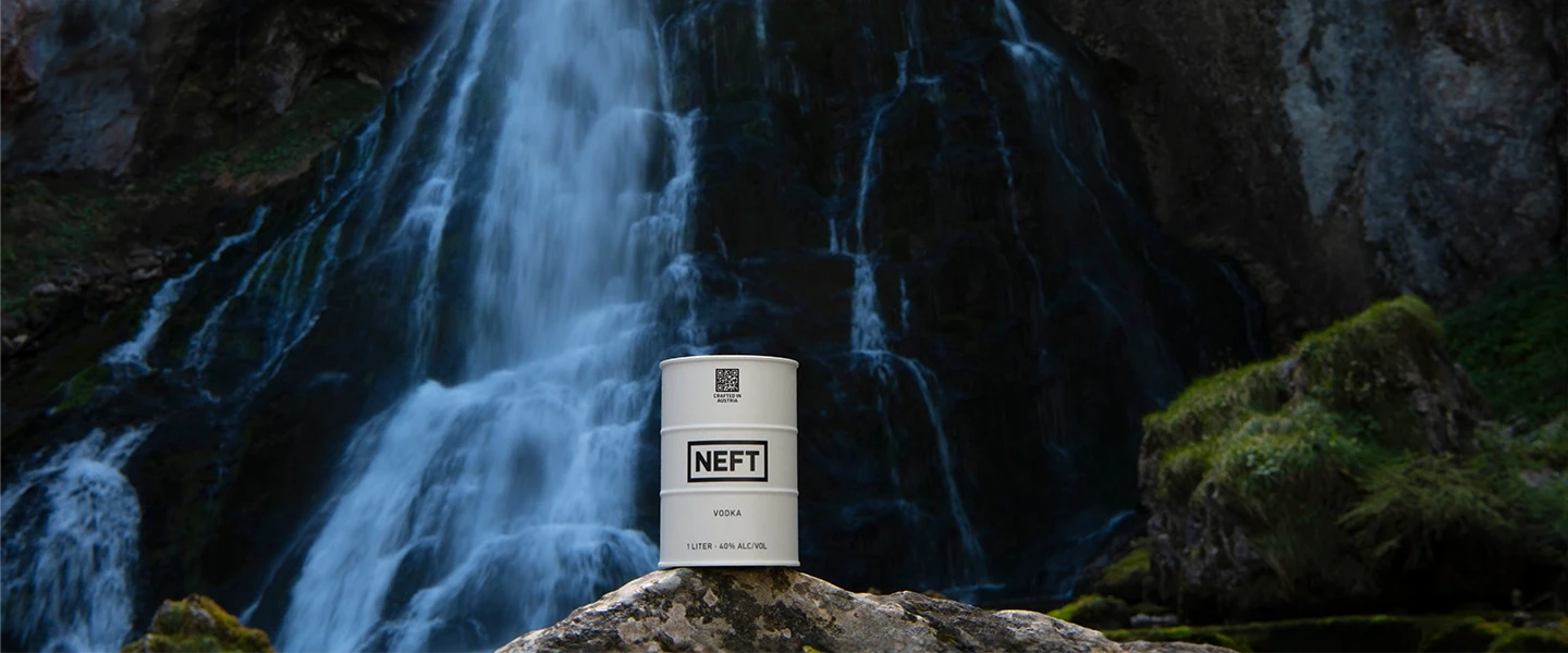 A NEFT Vodka white barrel in front of a rushing waterfall.