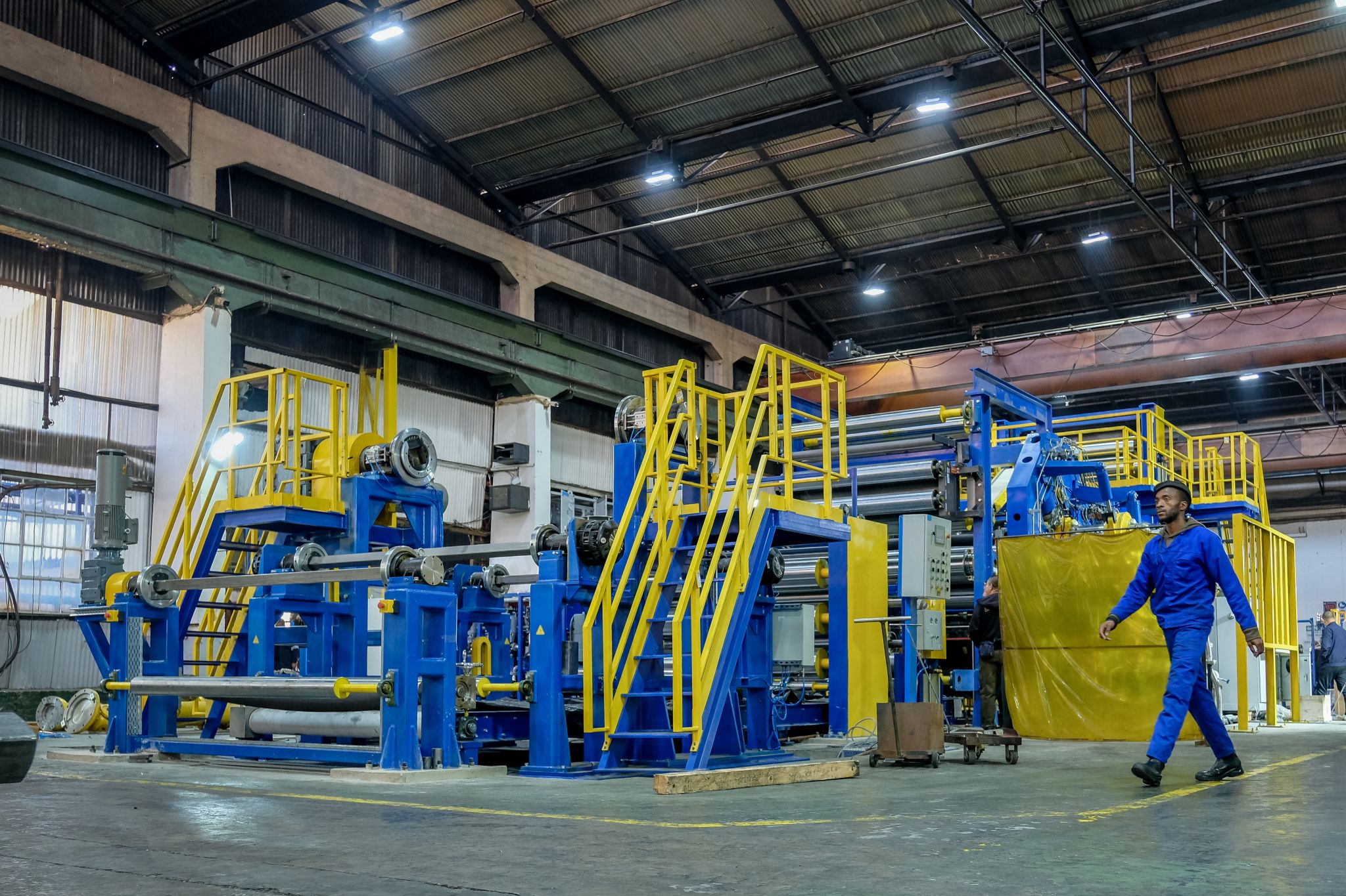 A smiling young man with crossed arms, wearing a plaid shirt and white t-shirt, poses against a dark background.