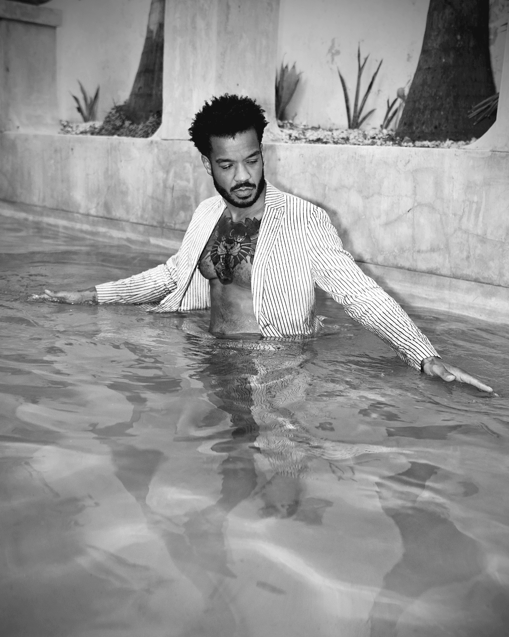 Man in linen suit in pool with woman hoisted dripping water with dress on