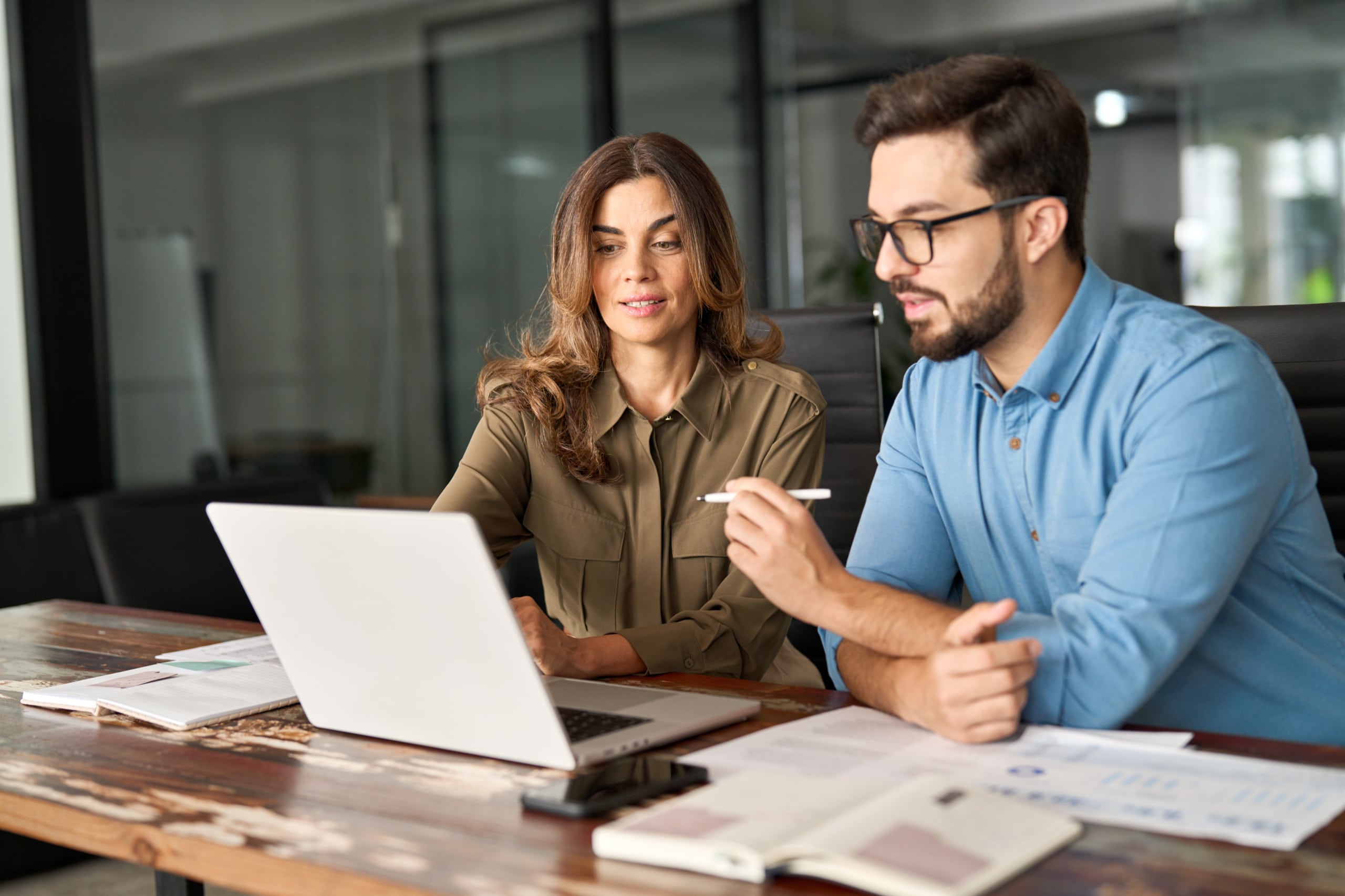 Two busy colleagues working together talking using laptop in office