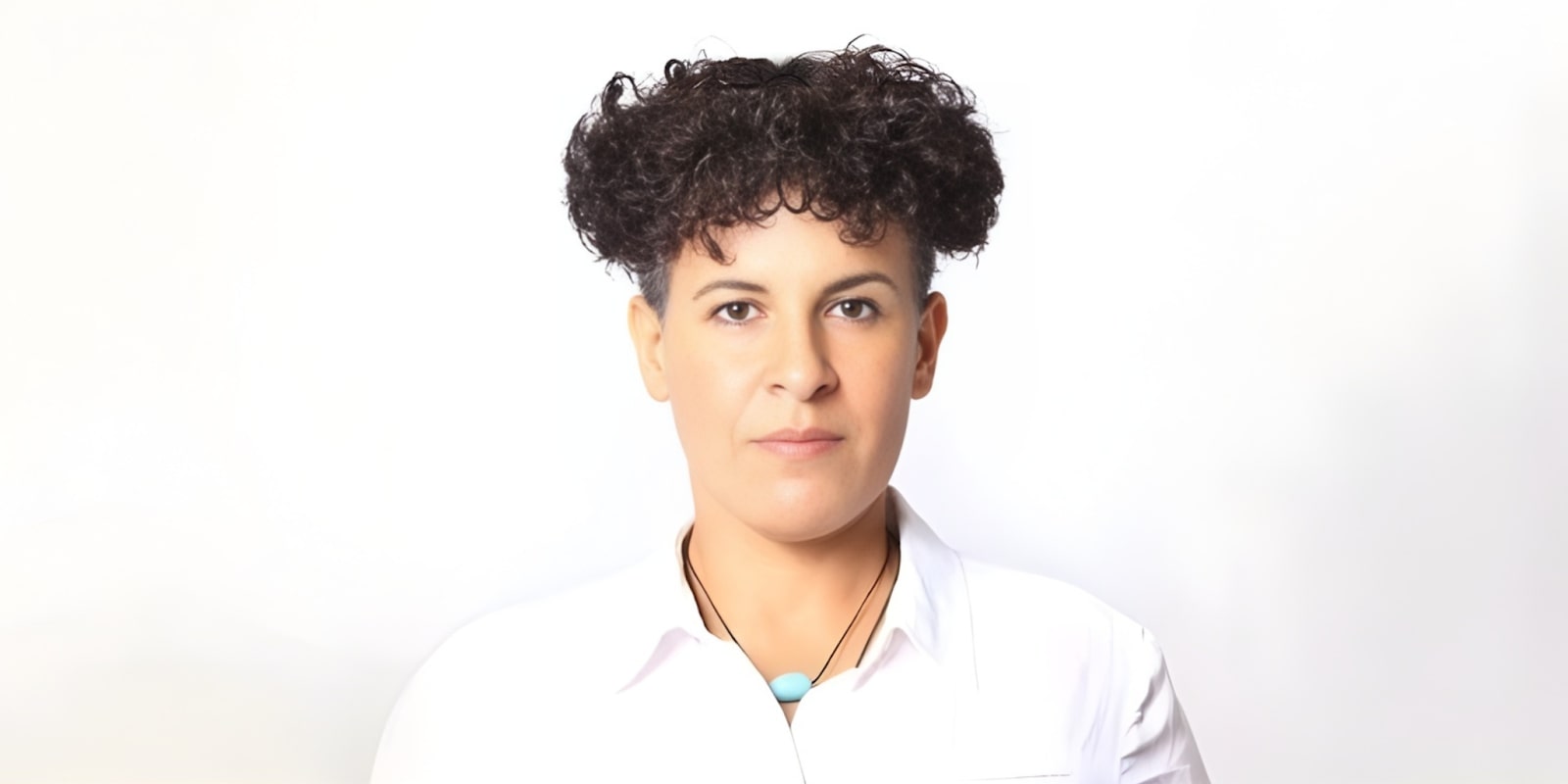 Naima Nouidjem, a professional coach, with curly hair, a serious expression, and a white shirt.