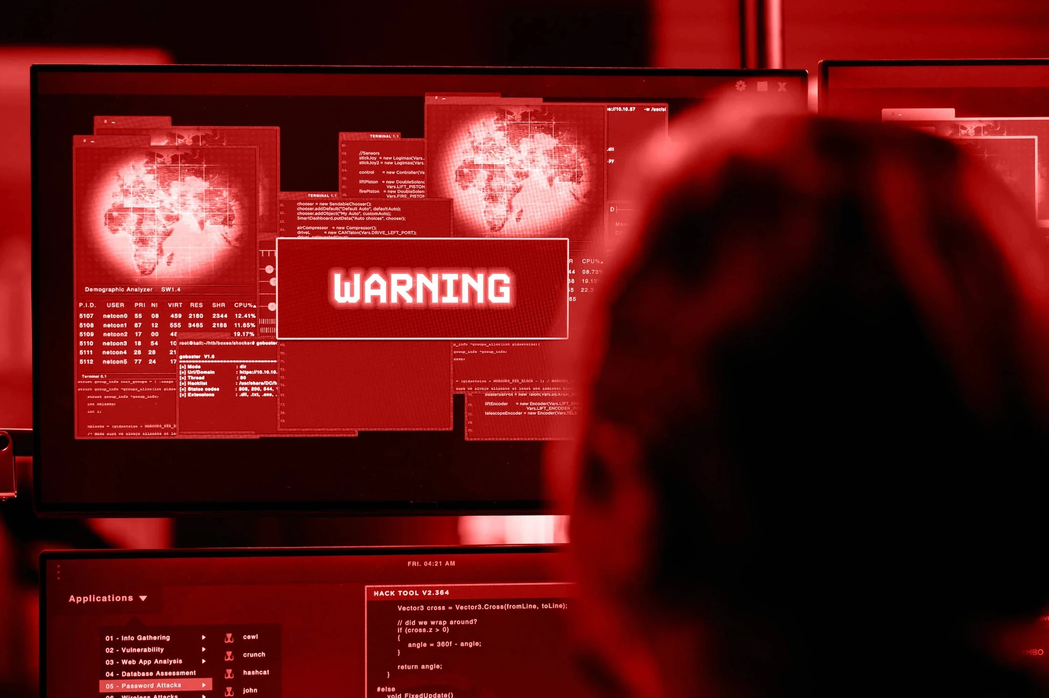 A control room with large monitors displaying data, illuminated with red lighting and featuring two seated operators.