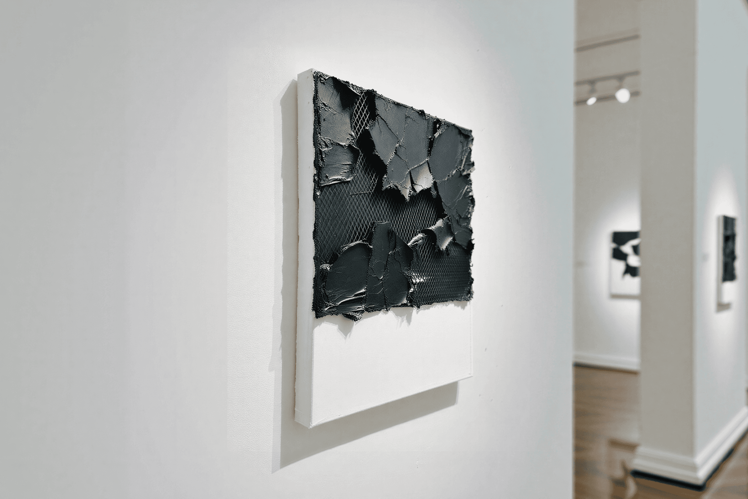 Modern art piece with textured black material on a white canvas, featuring a rugged, three-dimensional design with mesh patterns.